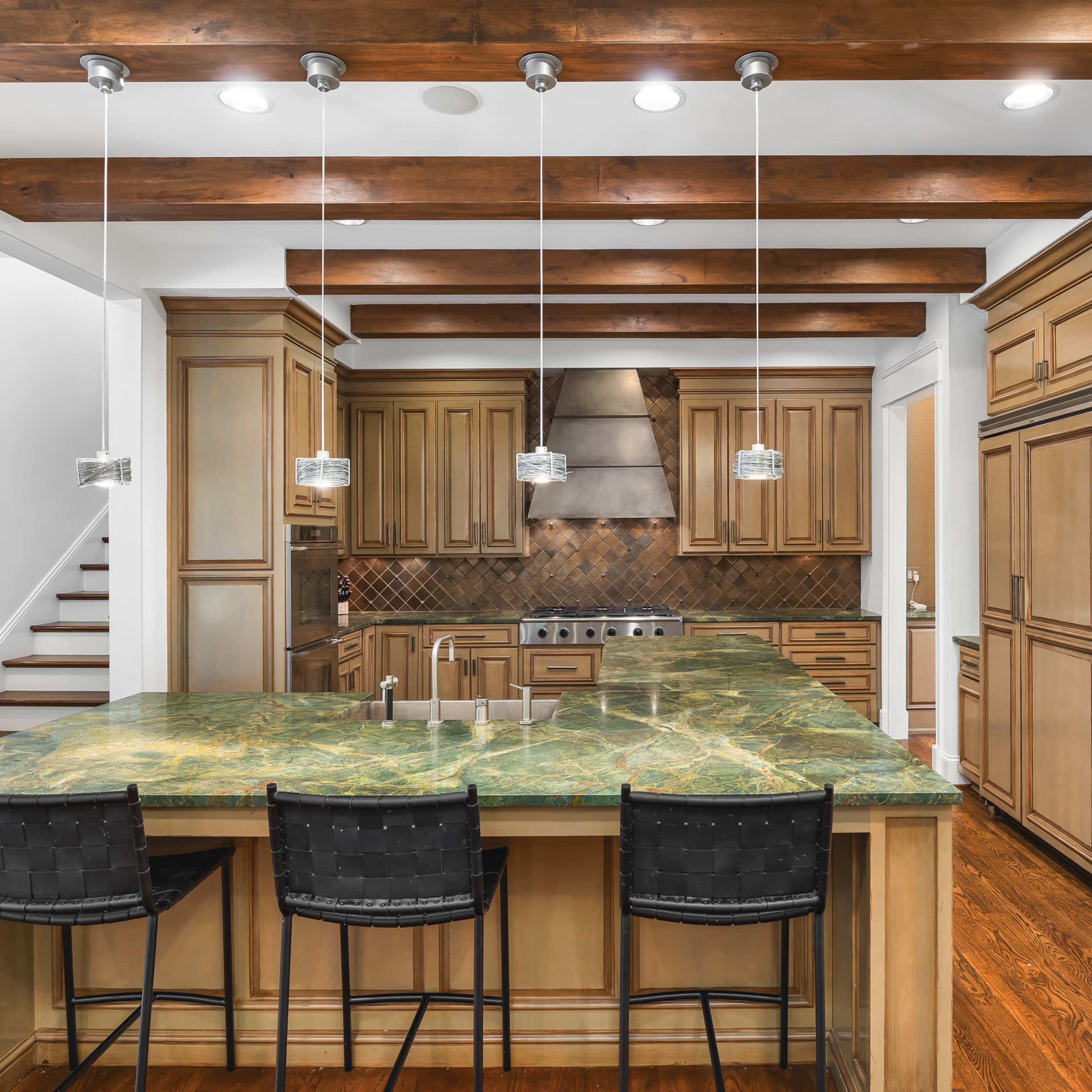 A spacious kitchen with wooden beams, green marble countertops, and several cabinets.