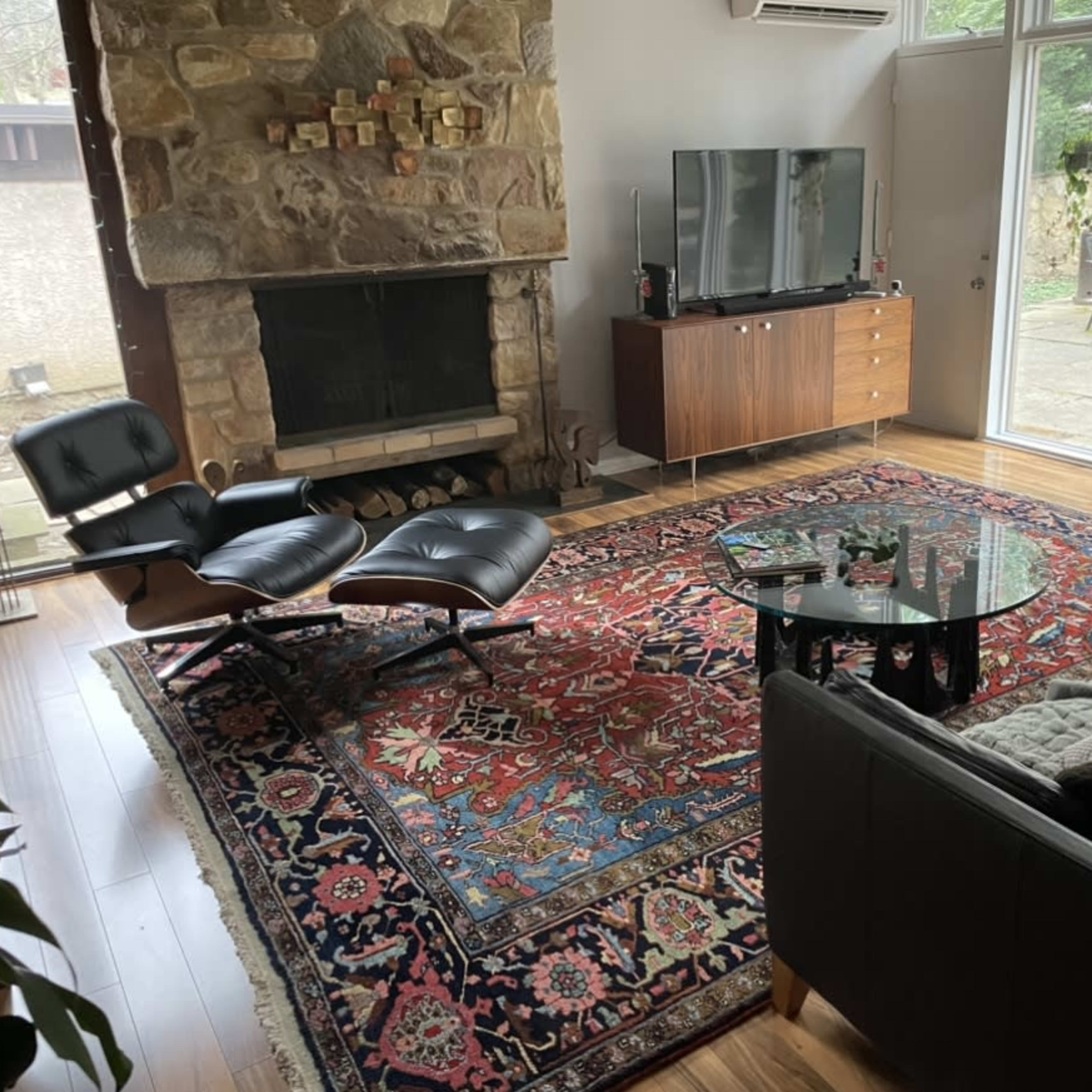 The living room features a stone fireplace, a television on a wooden cabinet, and modern black furniture arranged around a patterned area rug.
