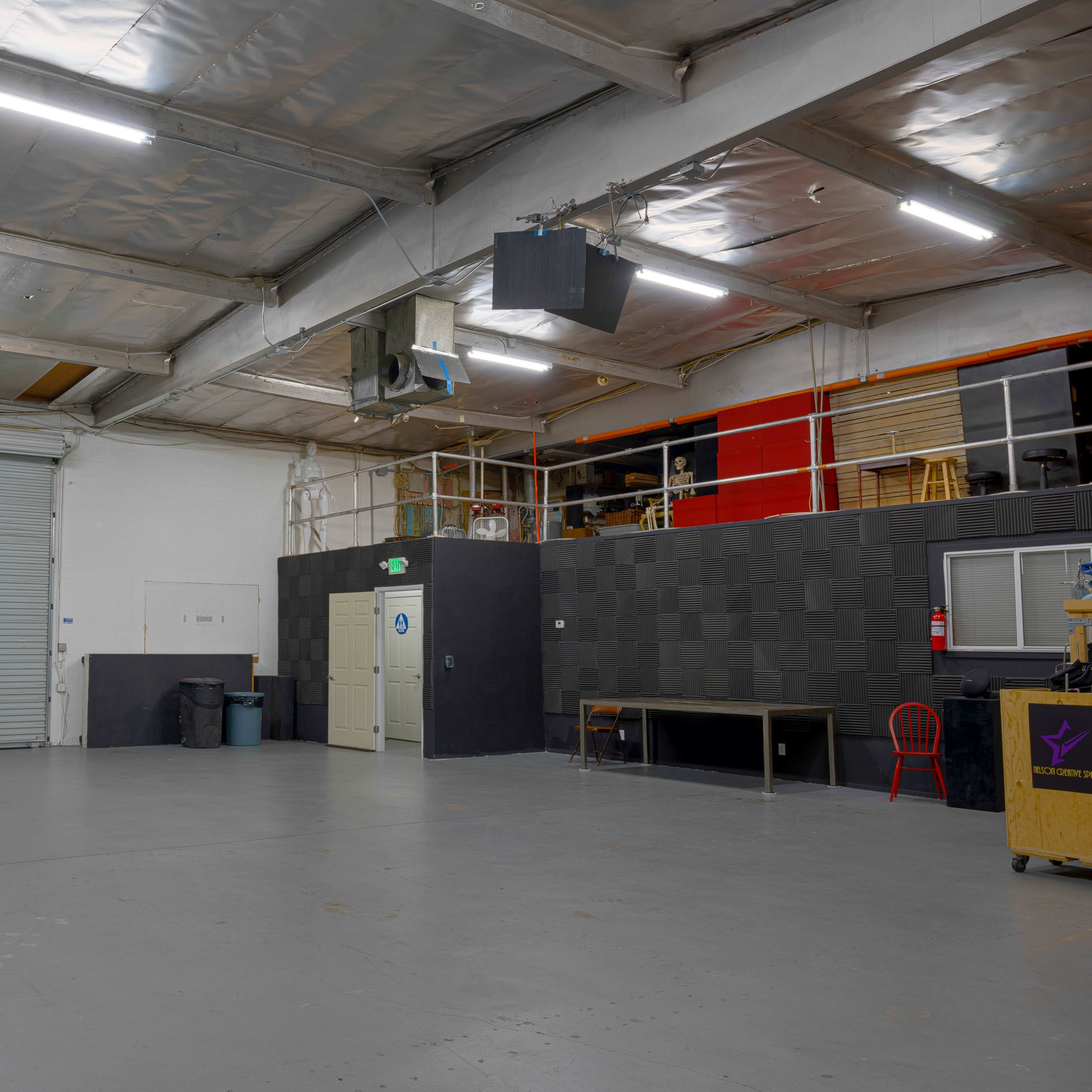 An empty warehouse space with a metallic roll-up door, a small table, and storage areas in the background.