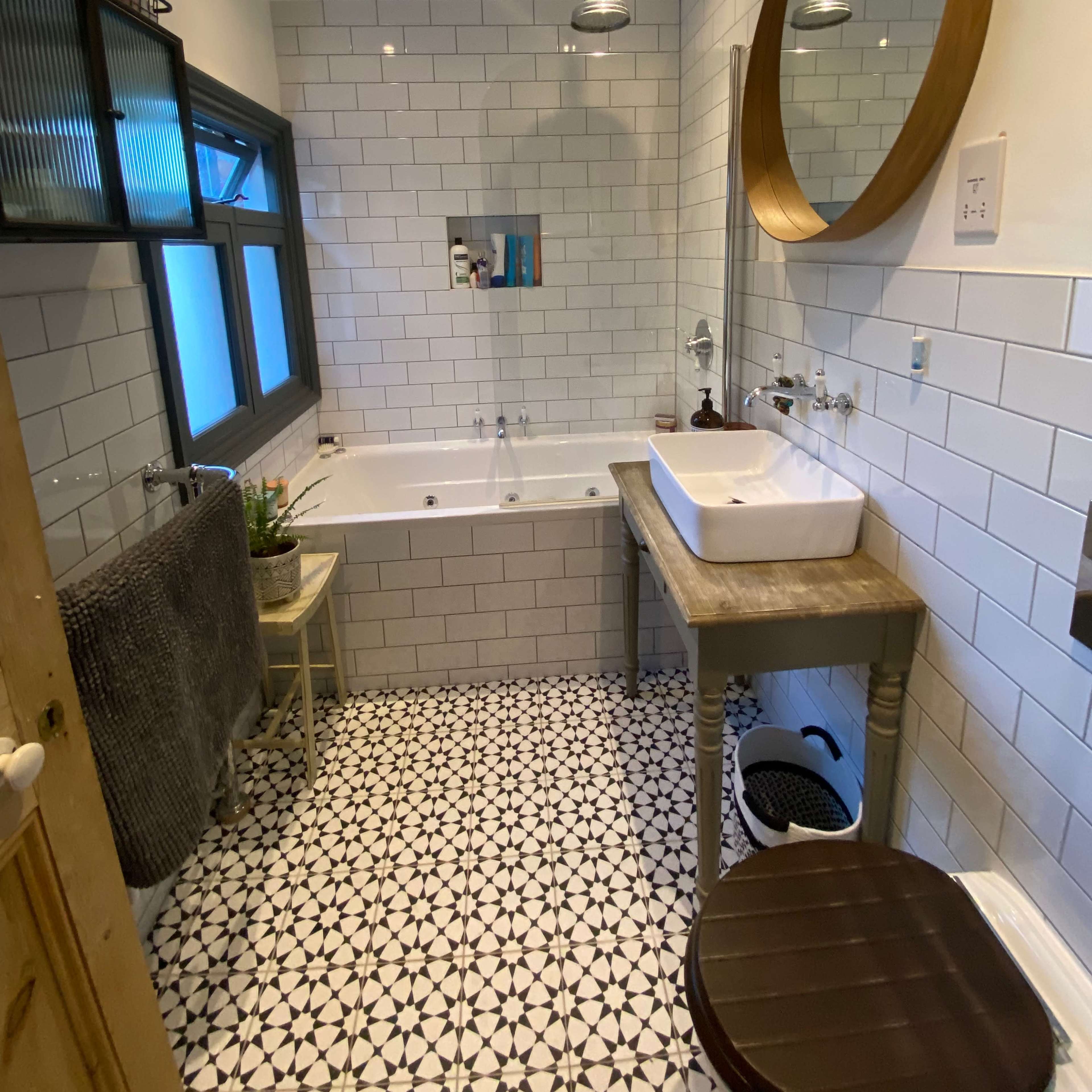The bathroom features a bathtub, sink, and modern fixtures with white tiled walls and patterned floor tiles.
