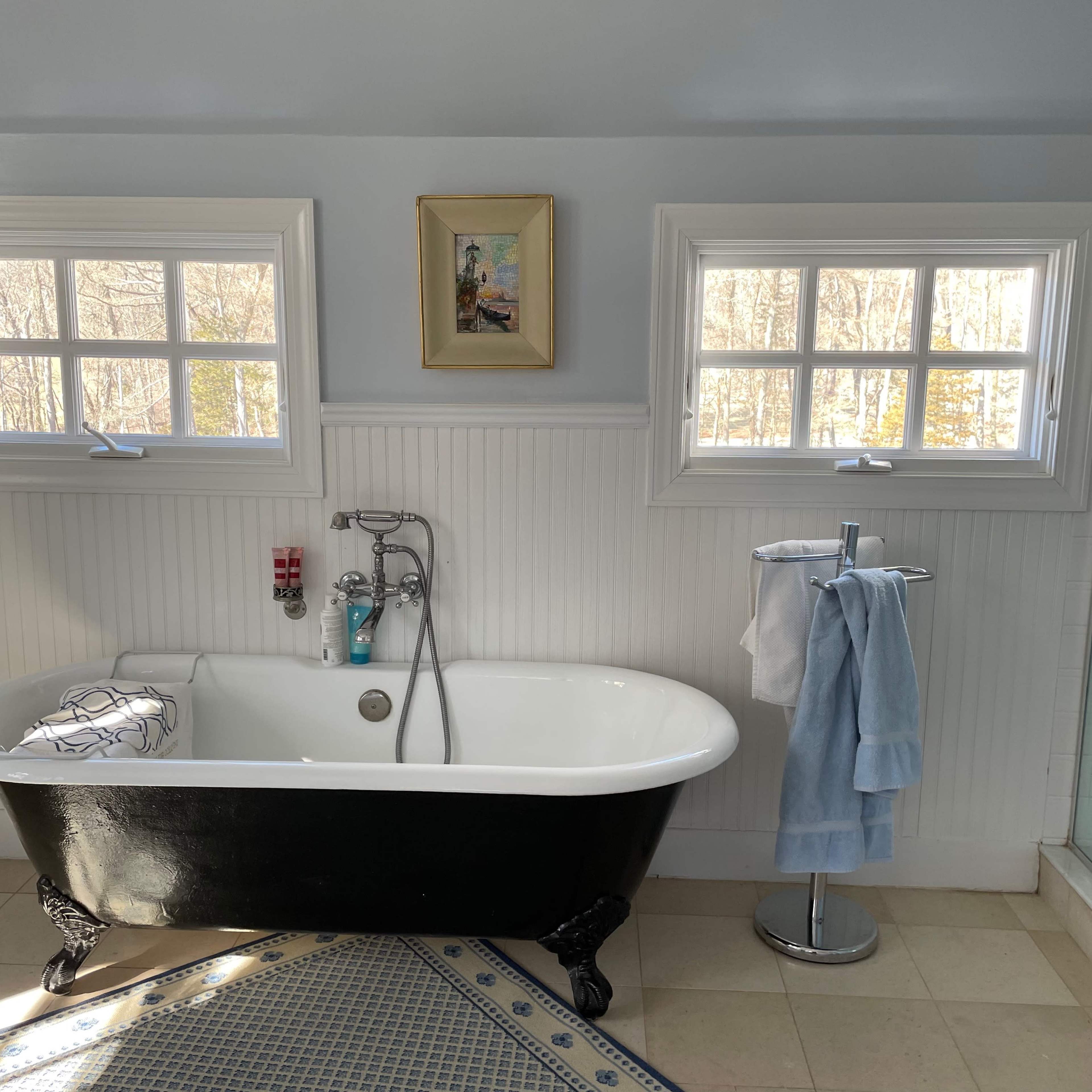 A bath area featuring a vintage black and white clawfoot tub, two windows allowing natural light, and a towel stand with towels.