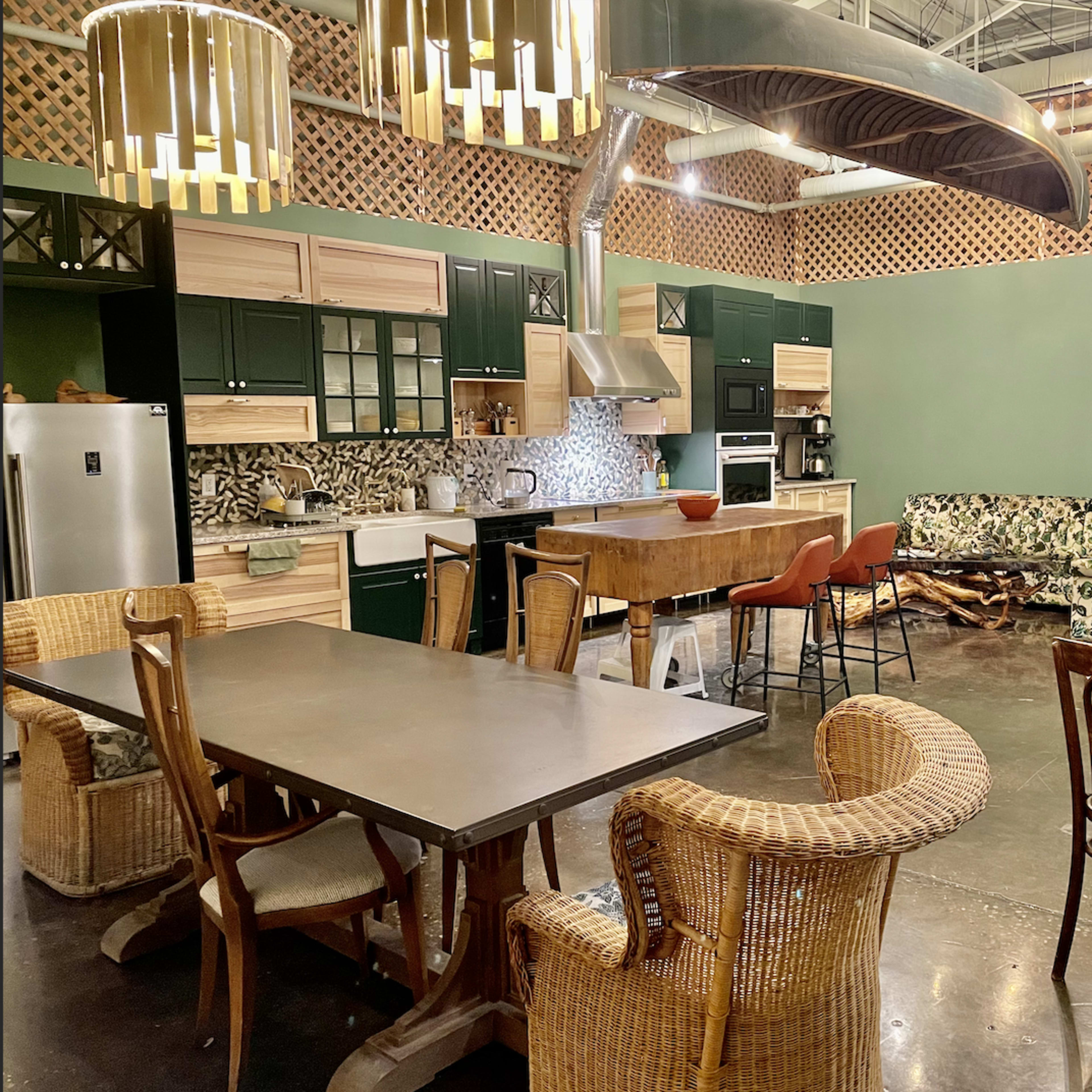 A spacious kitchen and dining area featuring modern furniture, a large table, and a colorful patterned sofa against a green wall.