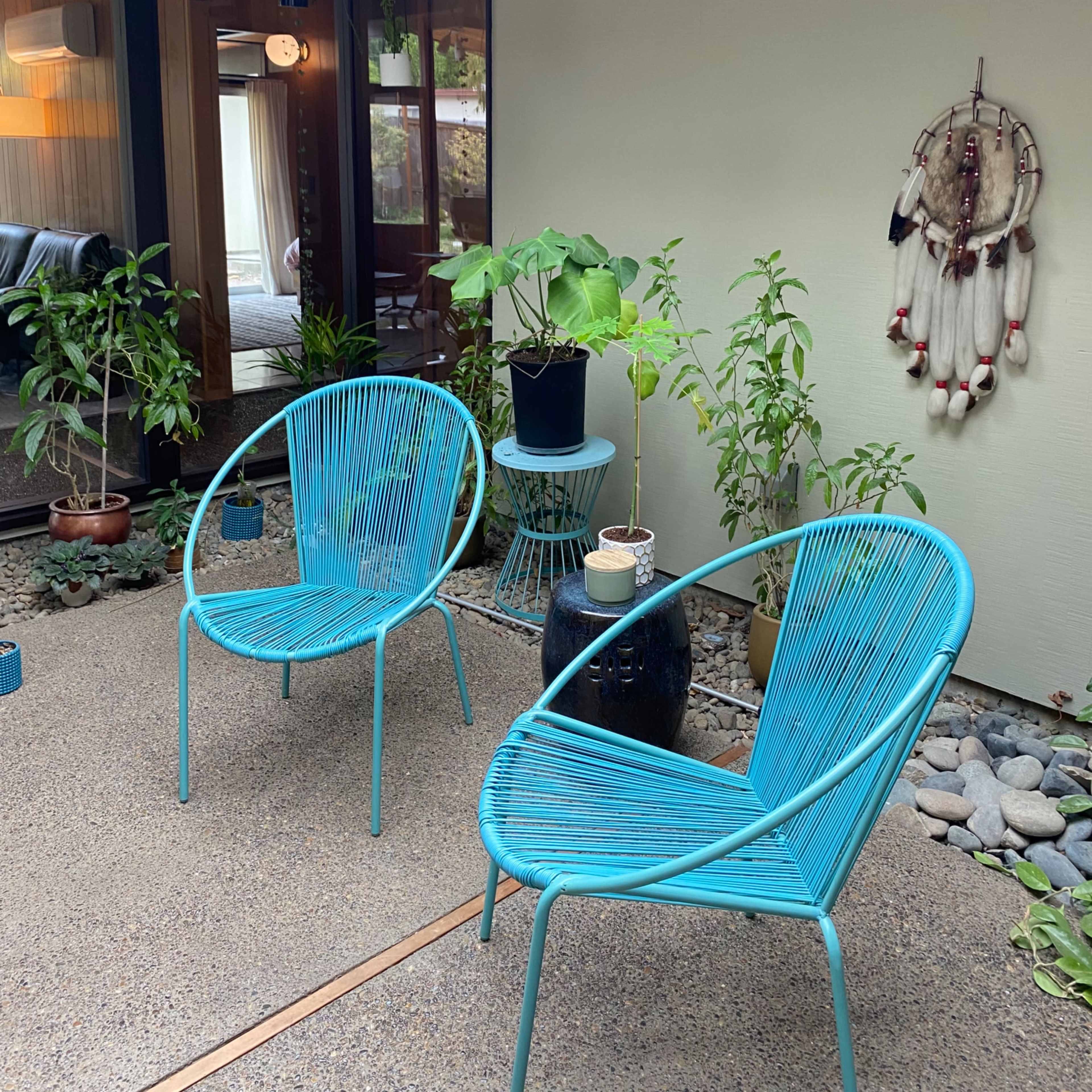 A small indoor courtyard with two turquoise chairs, potted plants, and decorative elements against a neutral wall.