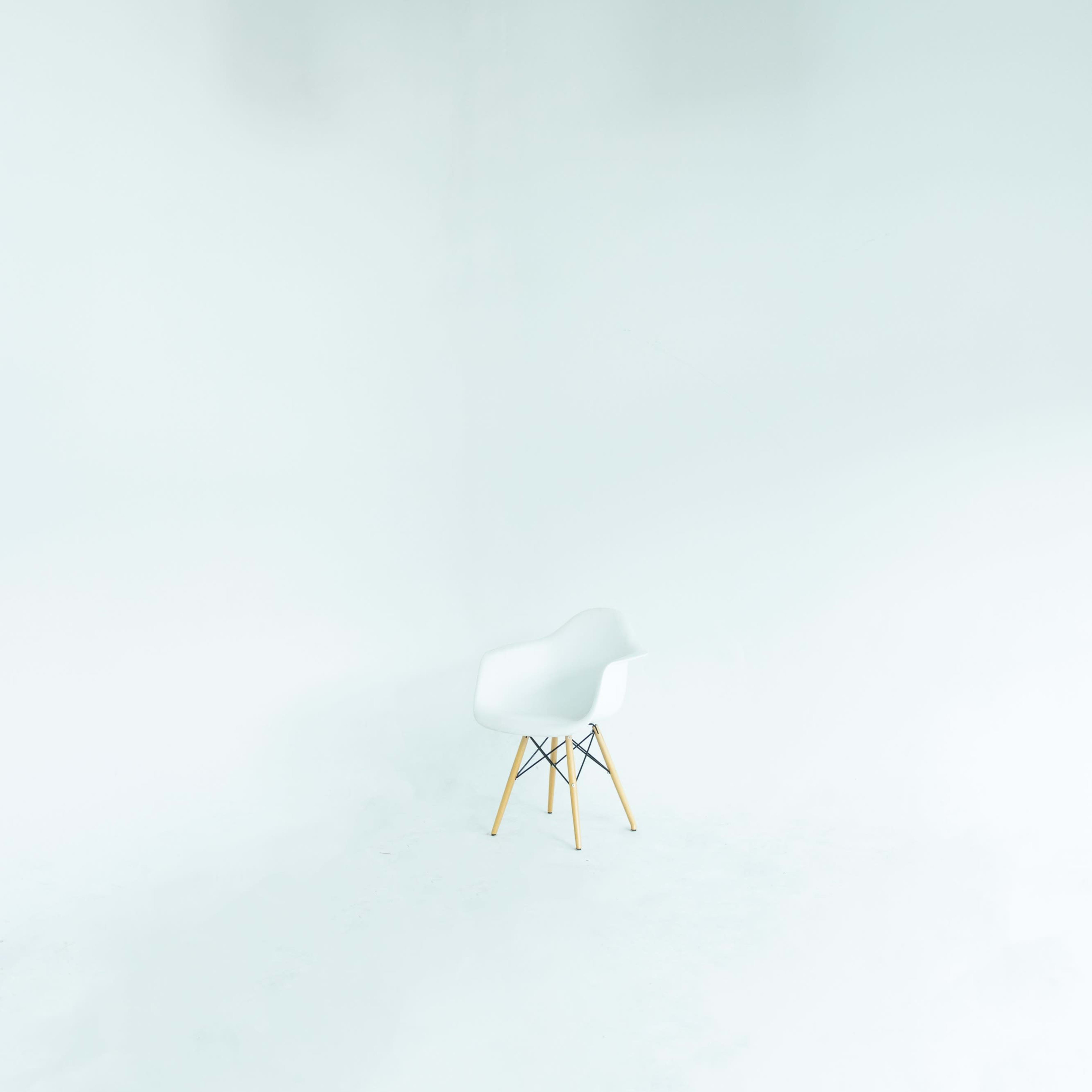 A white Eames chair is positioned in the center of a brightly lit, empty studio space with white walls.