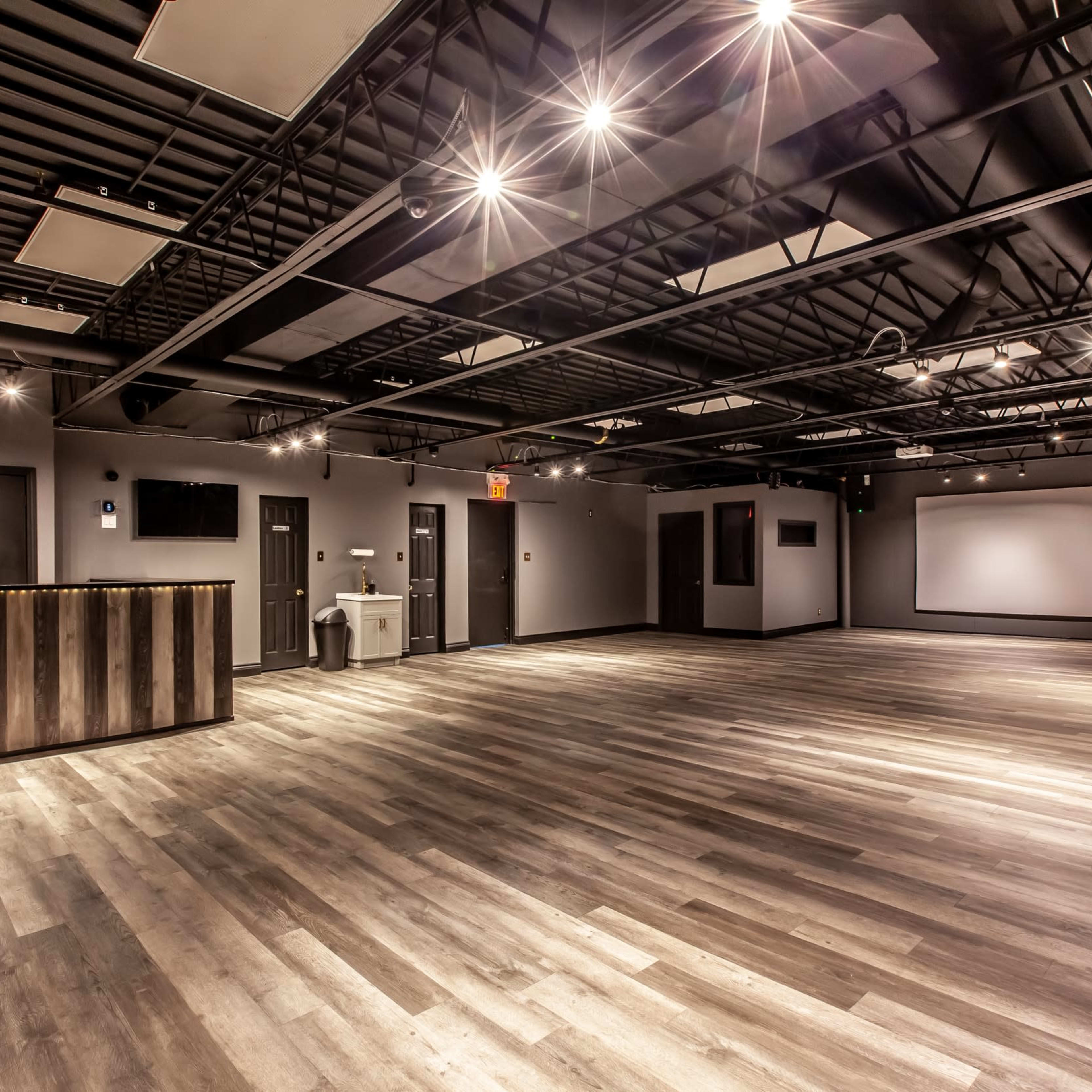 A spacious, modern interior room with wooden flooring, dim lighting, and a wooden reception counter.