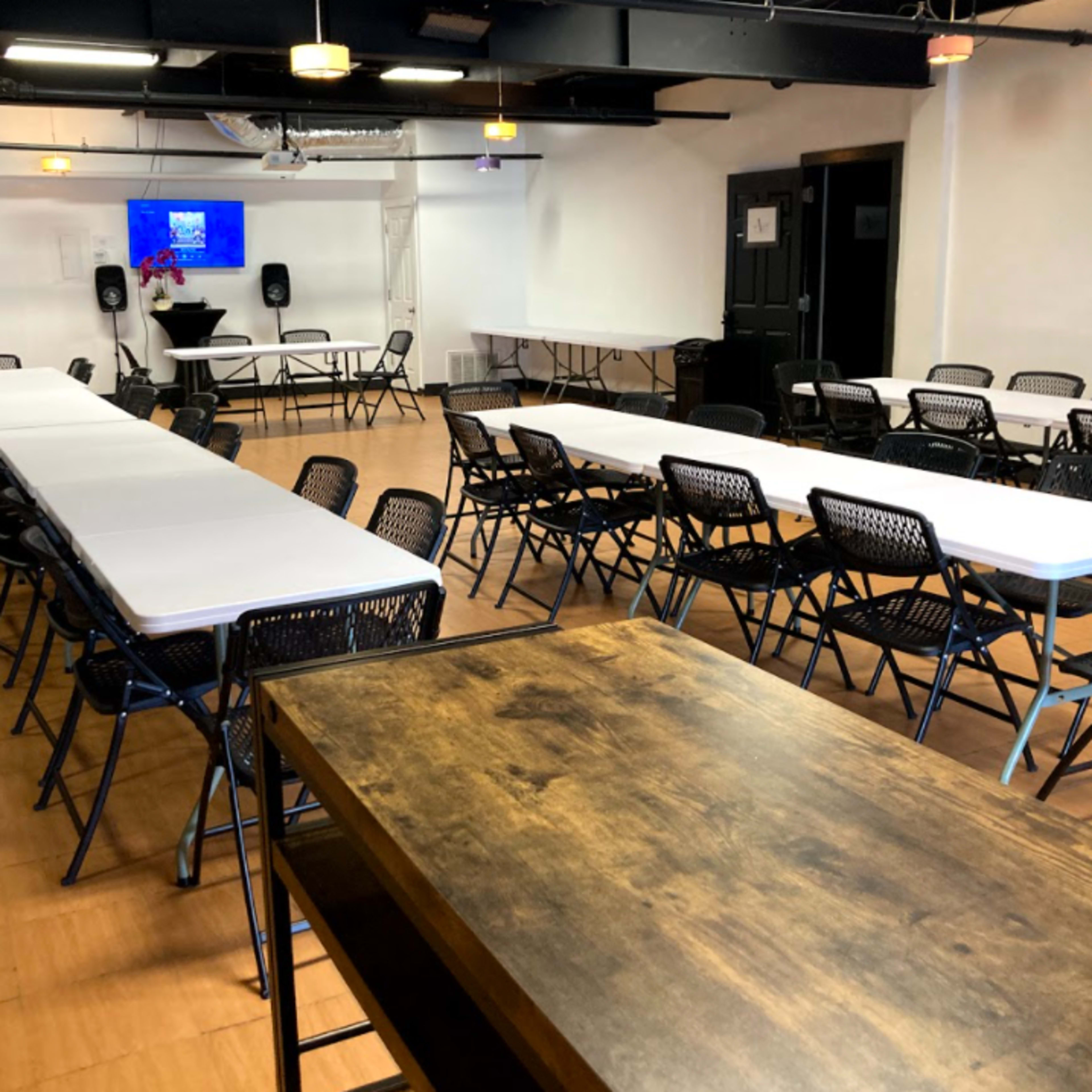 A spacious conference room features rows of folding tables and chairs arranged for an event, with a presentation screen at the front.