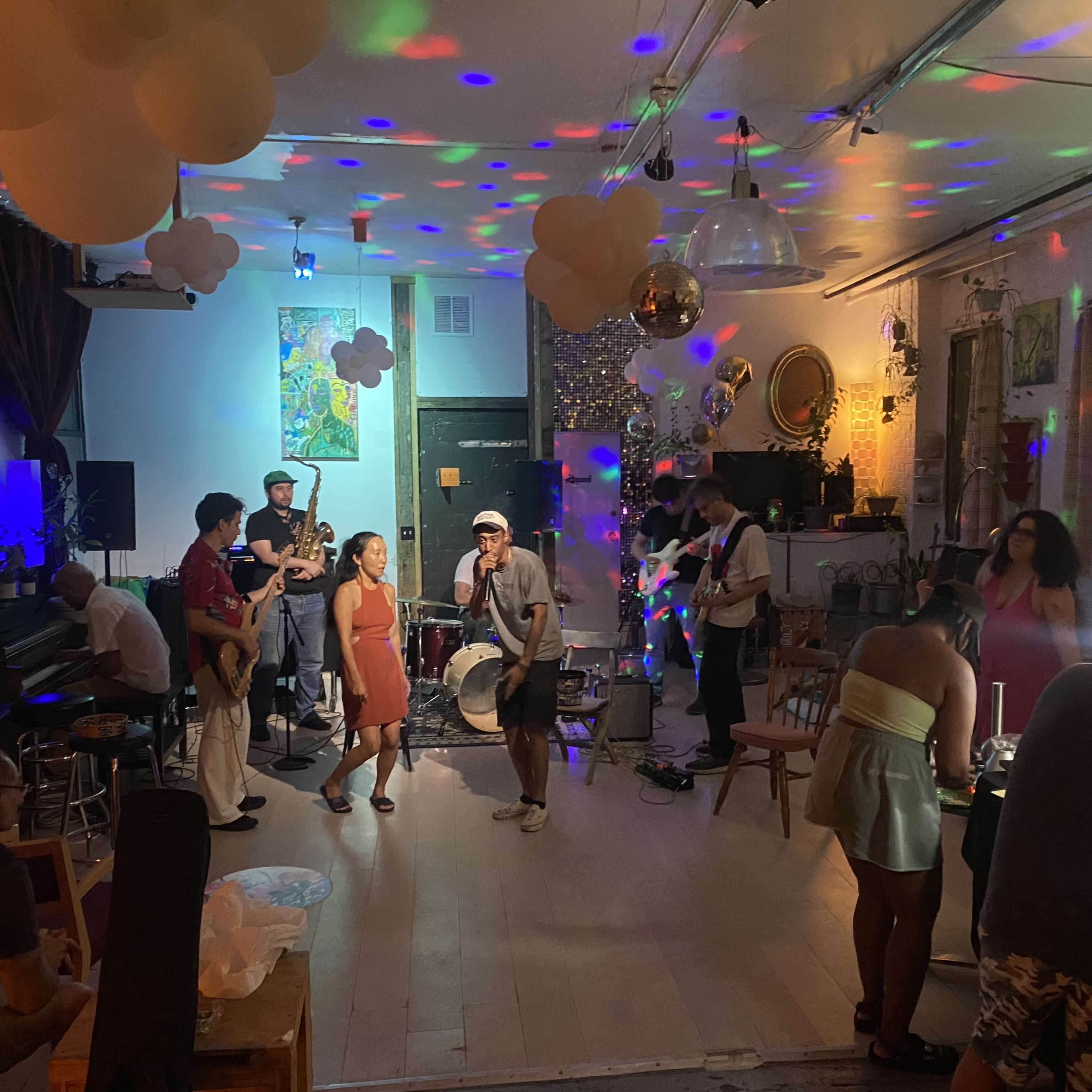 A diverse group of people performs music and socializes in a decorated indoor space with colorful lights and decorations for a lively gathering.