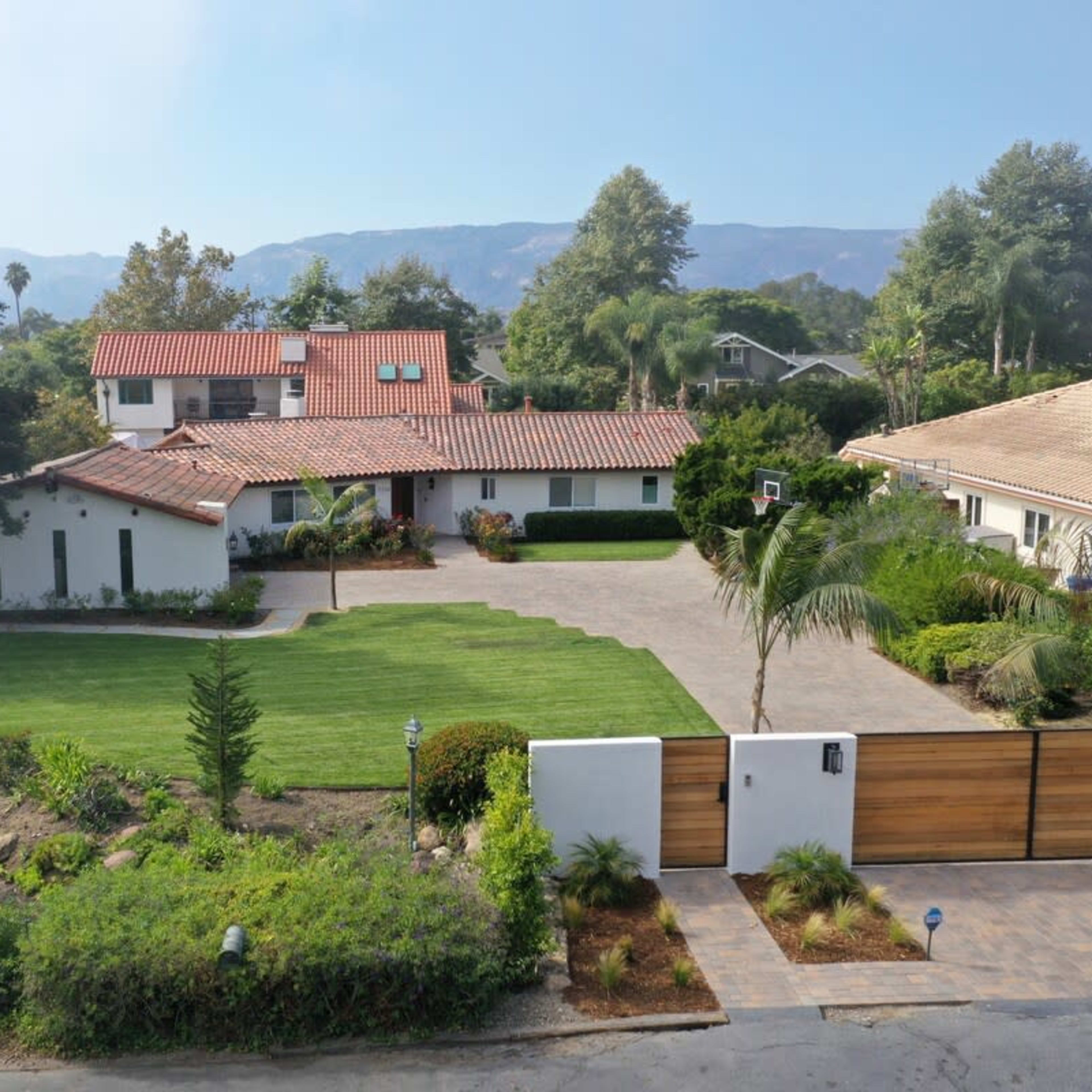 A spacious residential property featuring a landscaped yard, a paved driveway, and nearby mountains in the background.