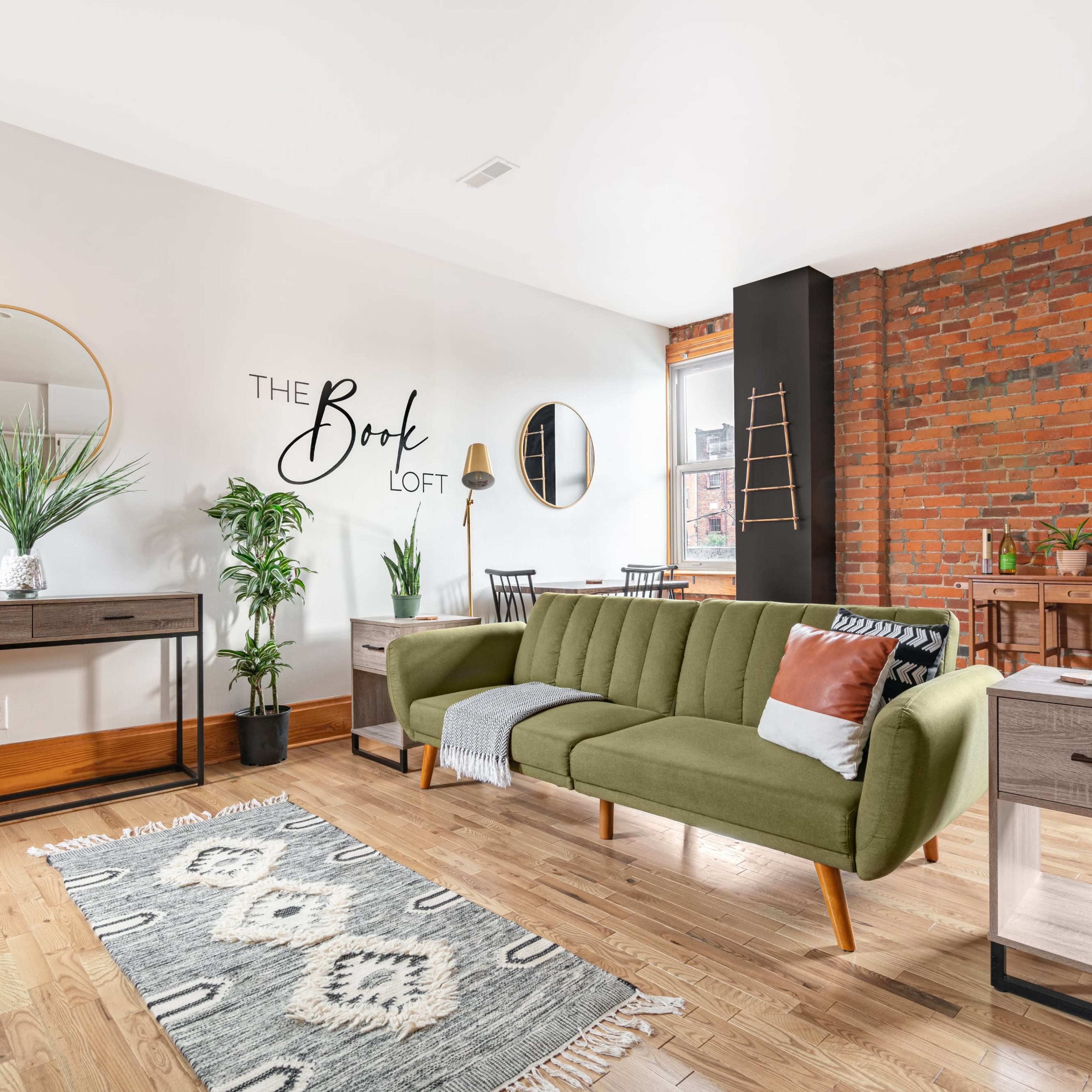 A modern living space featuring a green sofa, wooden furniture, potted plants, and a decorative wall saying "The Book Loft."