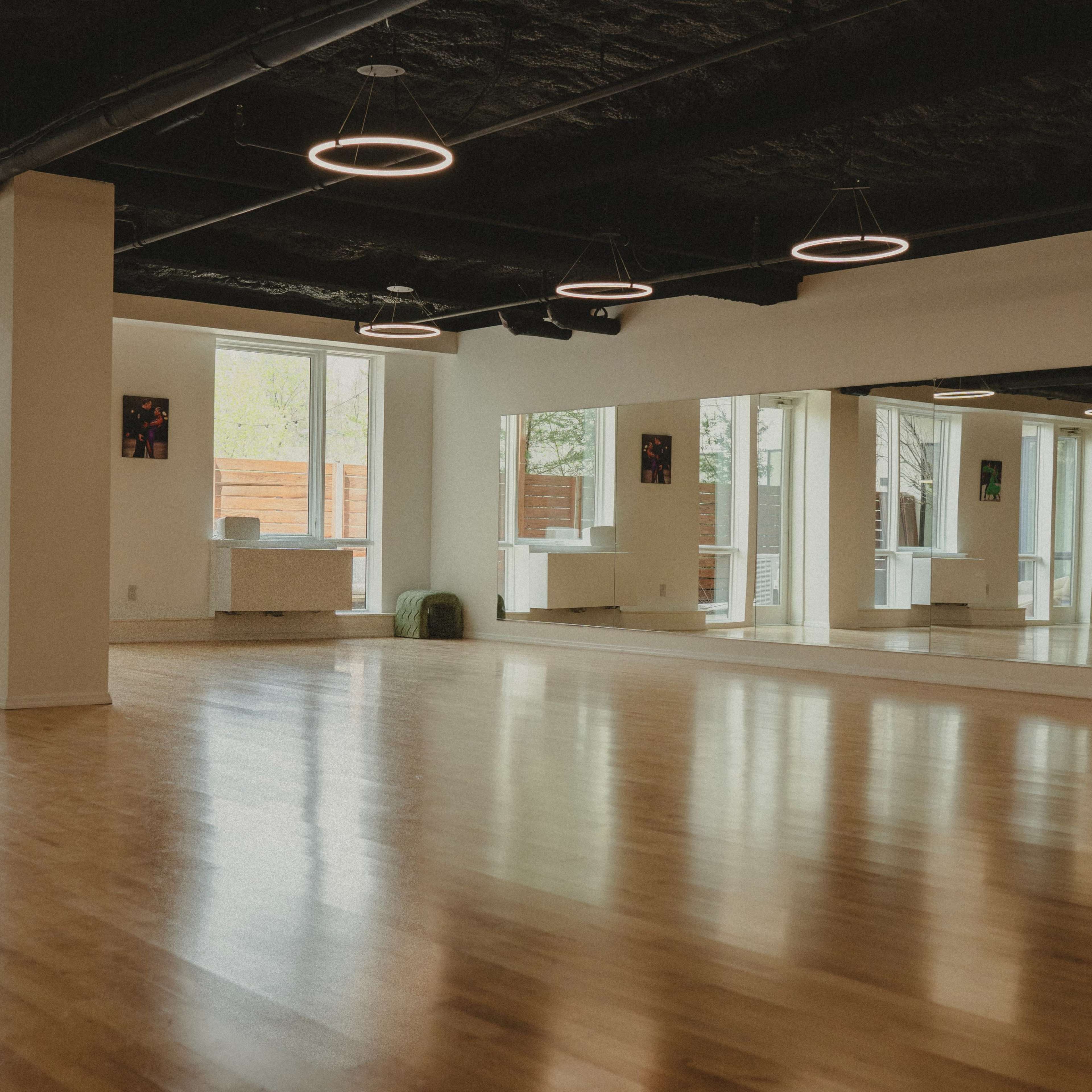A spacious, well-lit studio with hardwood flooring and several large windows.