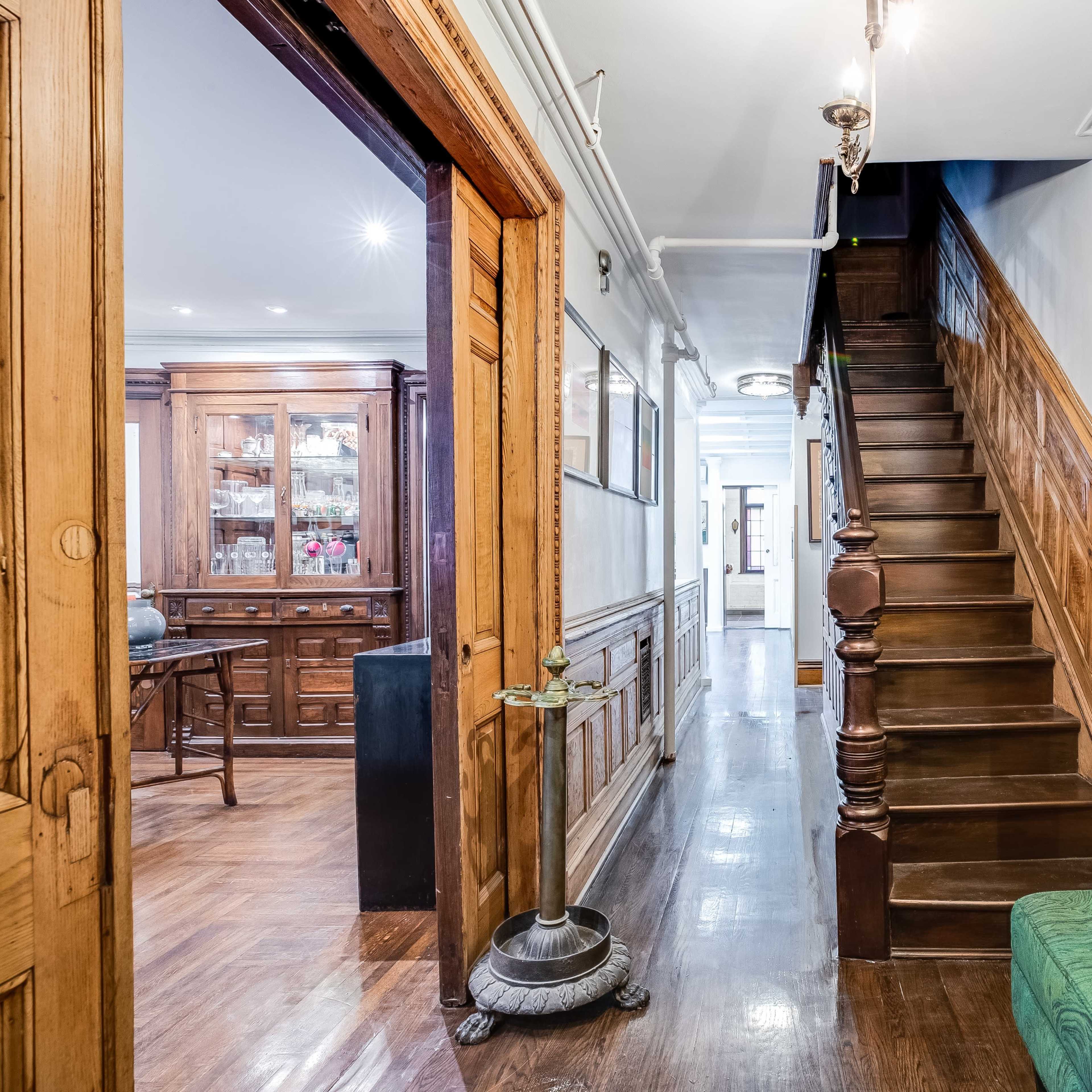 A wooden hallway leading to a staircase, with a green bench on the right and an ornate banister along the stairs.