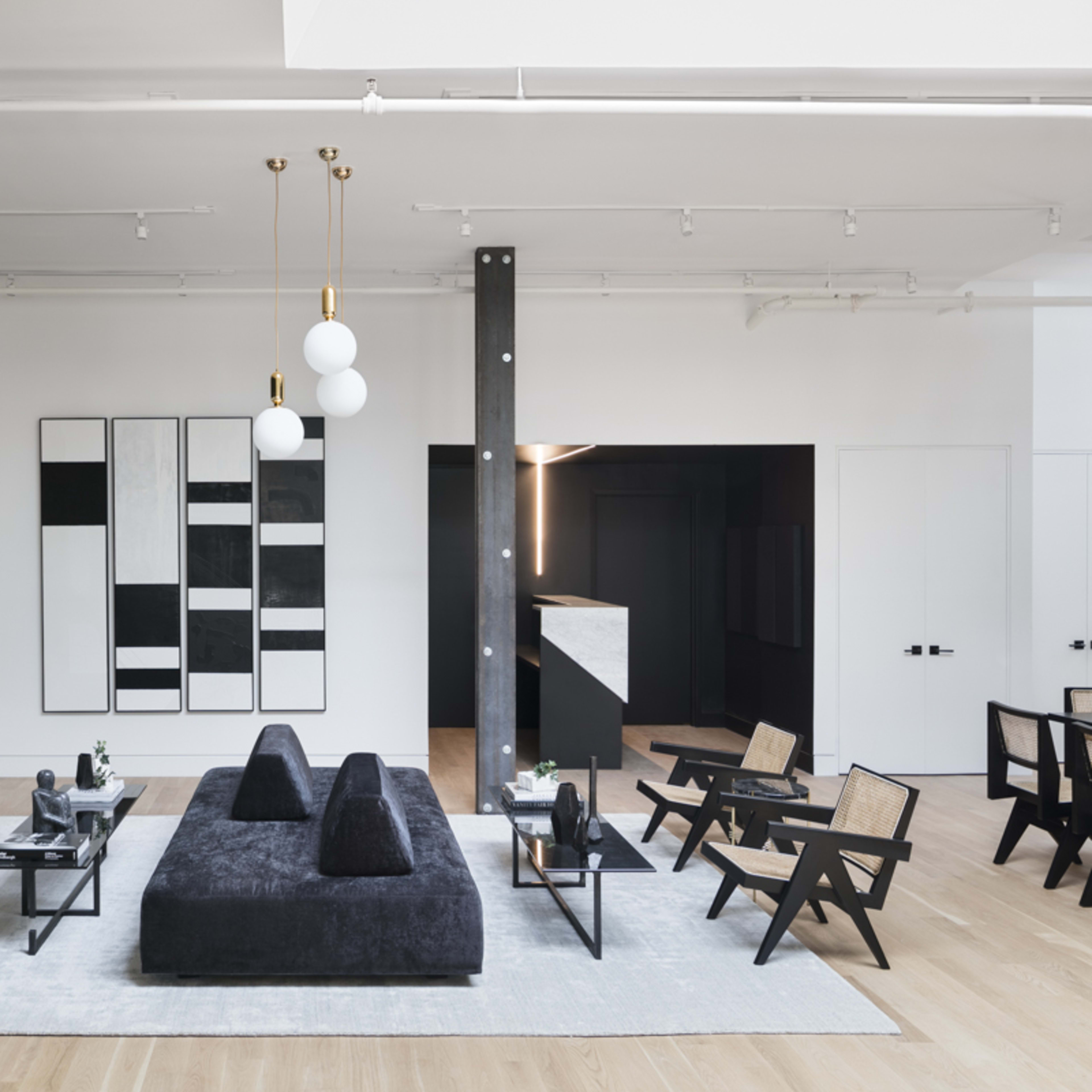 A modern interior space features a central dark sofa surrounded by unique wooden chairs and artwork on the walls, with an open layout that includes a desk area in the background.