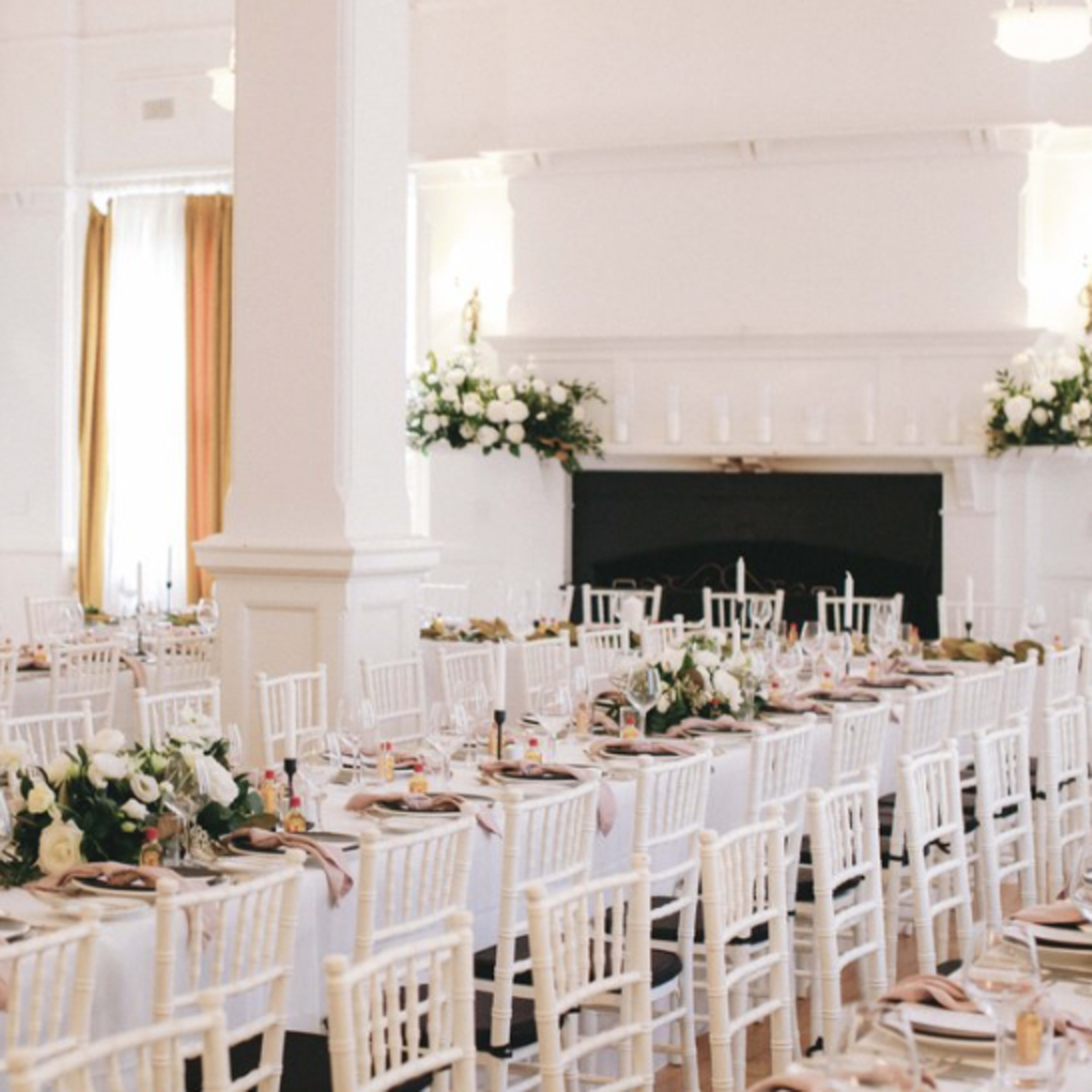 A banquet hall set for a formal dinner with white tables, chairs, and floral arrangements.