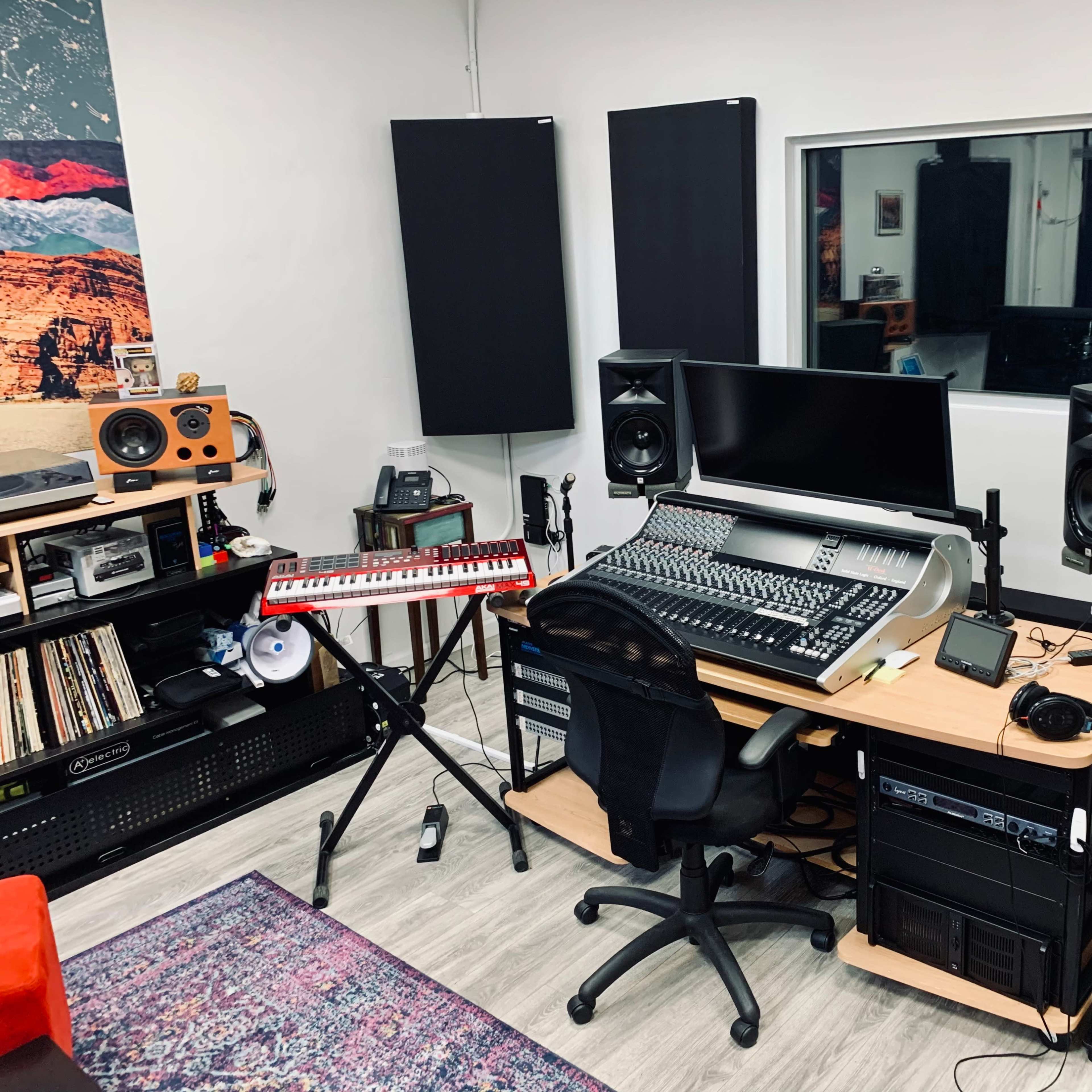 A modern music studio featuring a large sound mixing desk, studio monitors, a keyboard, and soundproof wall panels.