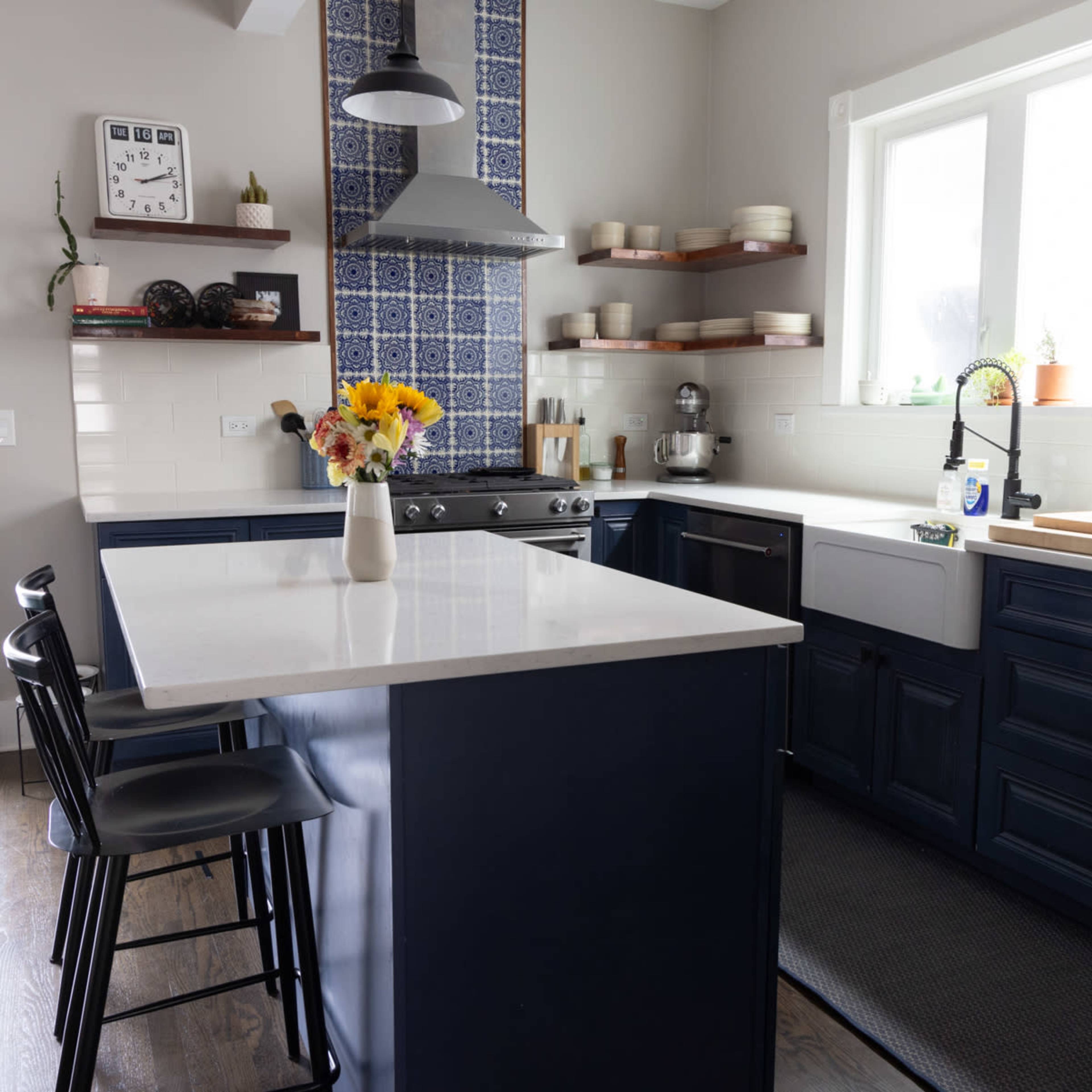 A modern kitchen features a blue cabinetry, a large white countertop island, and decorative wall tiles above the stove.