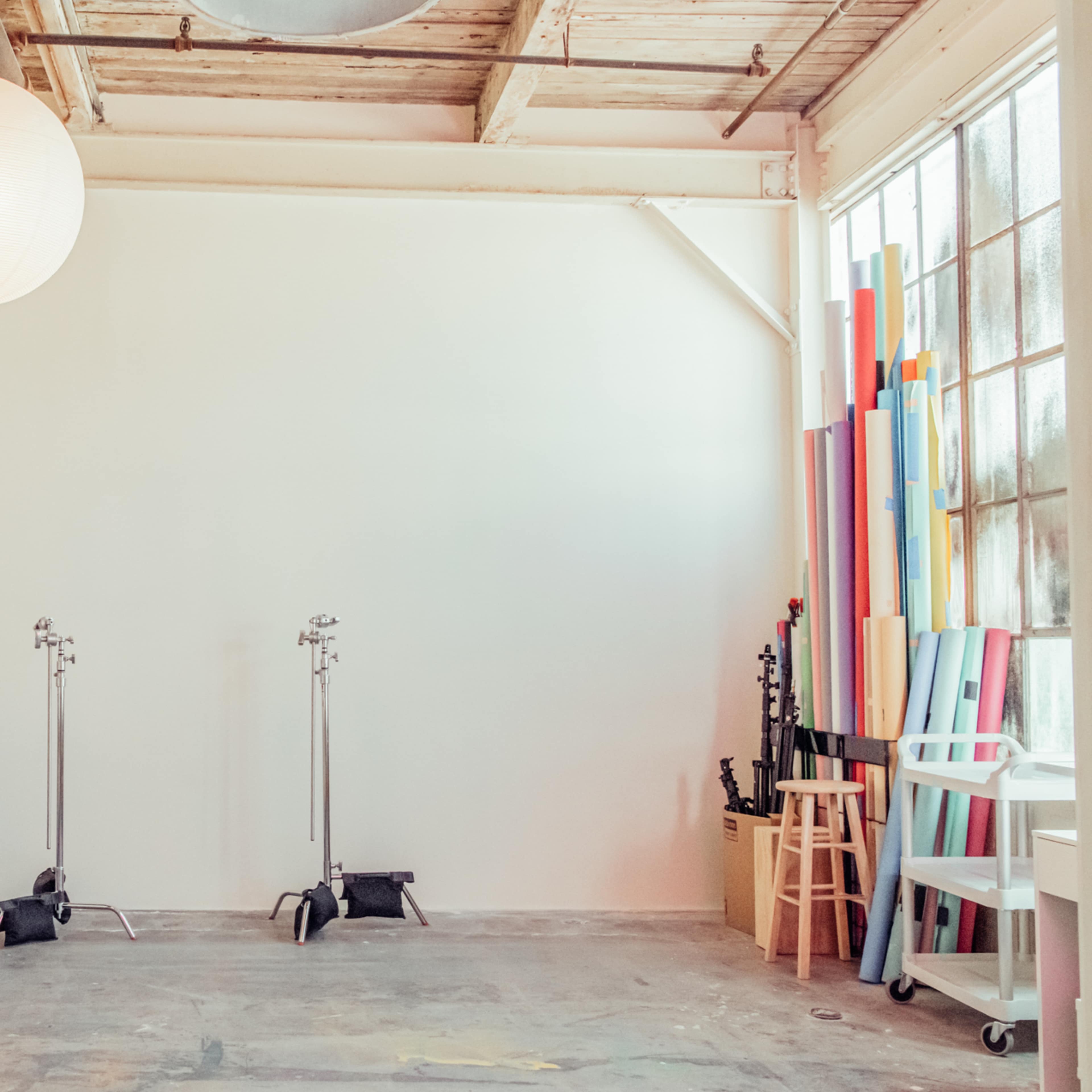 A spacious room with a white wall, a pink ladder, two light stands, colorful rolls of paper, and a couch in the corner.