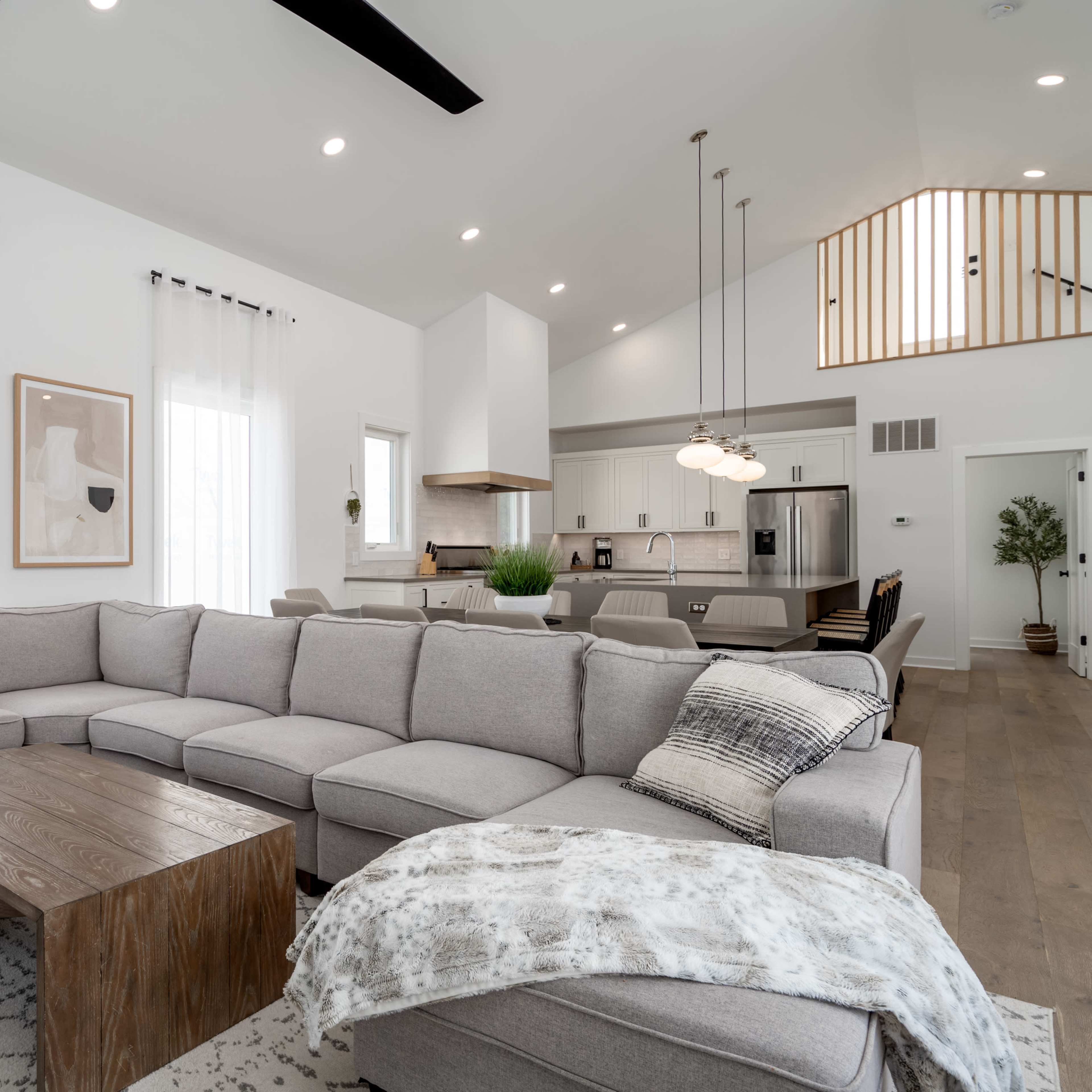 A spacious living room features a large gray sectional sofa, a wooden coffee table, and an open kitchen in the background.