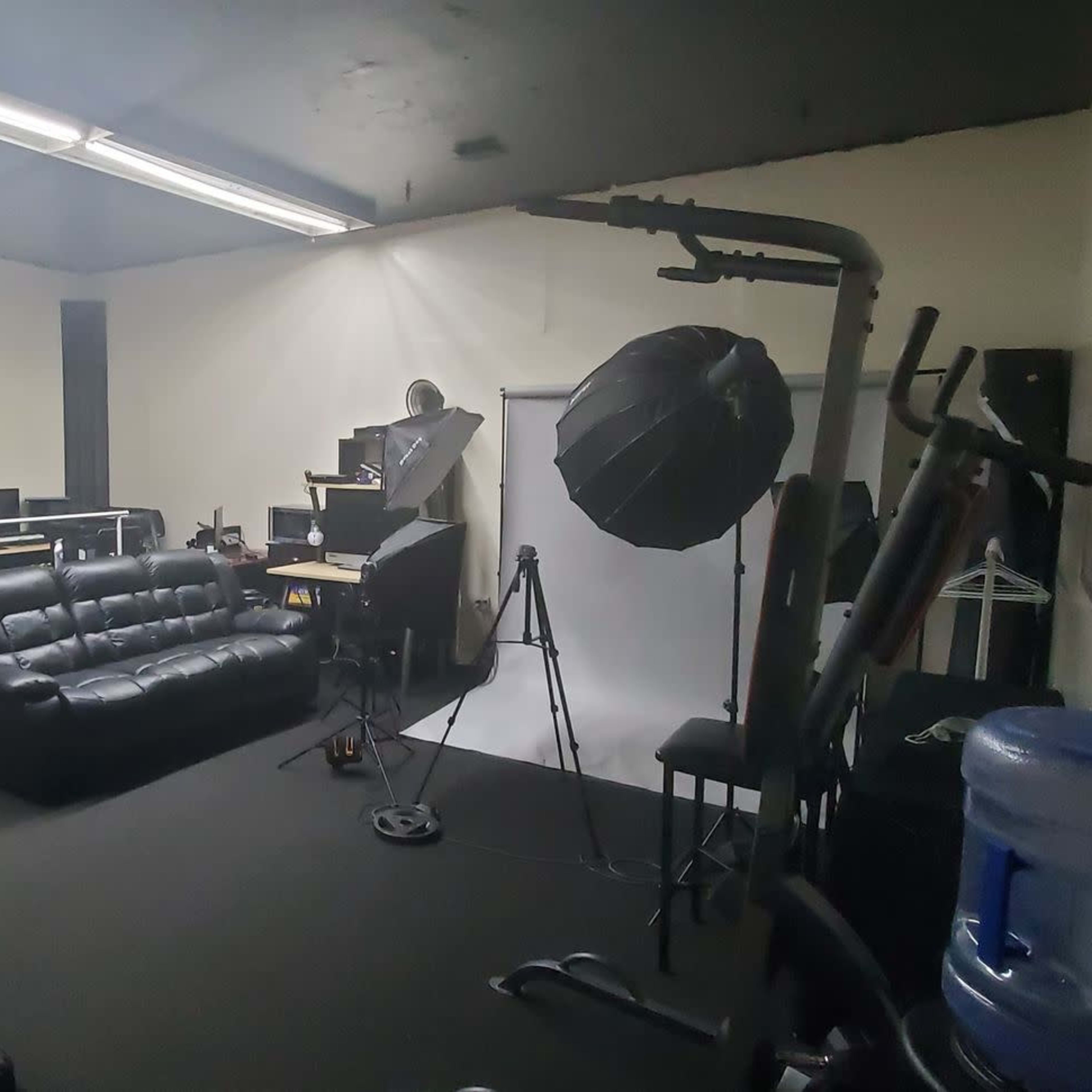 A studio room with black sofas, shelves, equipment, and a backdrop for photography or videography.