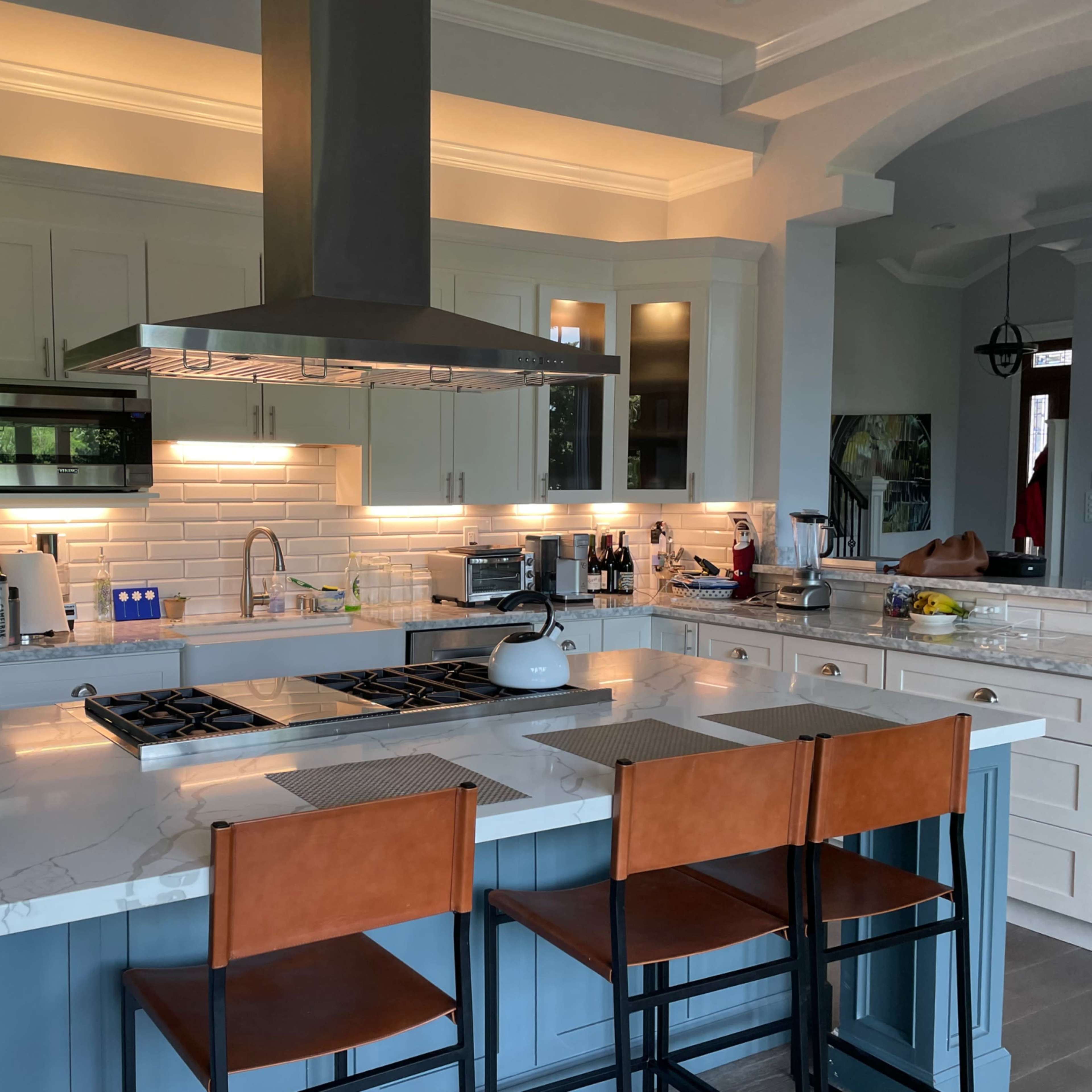 A modern kitchen features a central island with bar seating, stainless steel appliances, and a large vent hood above the cooktop.