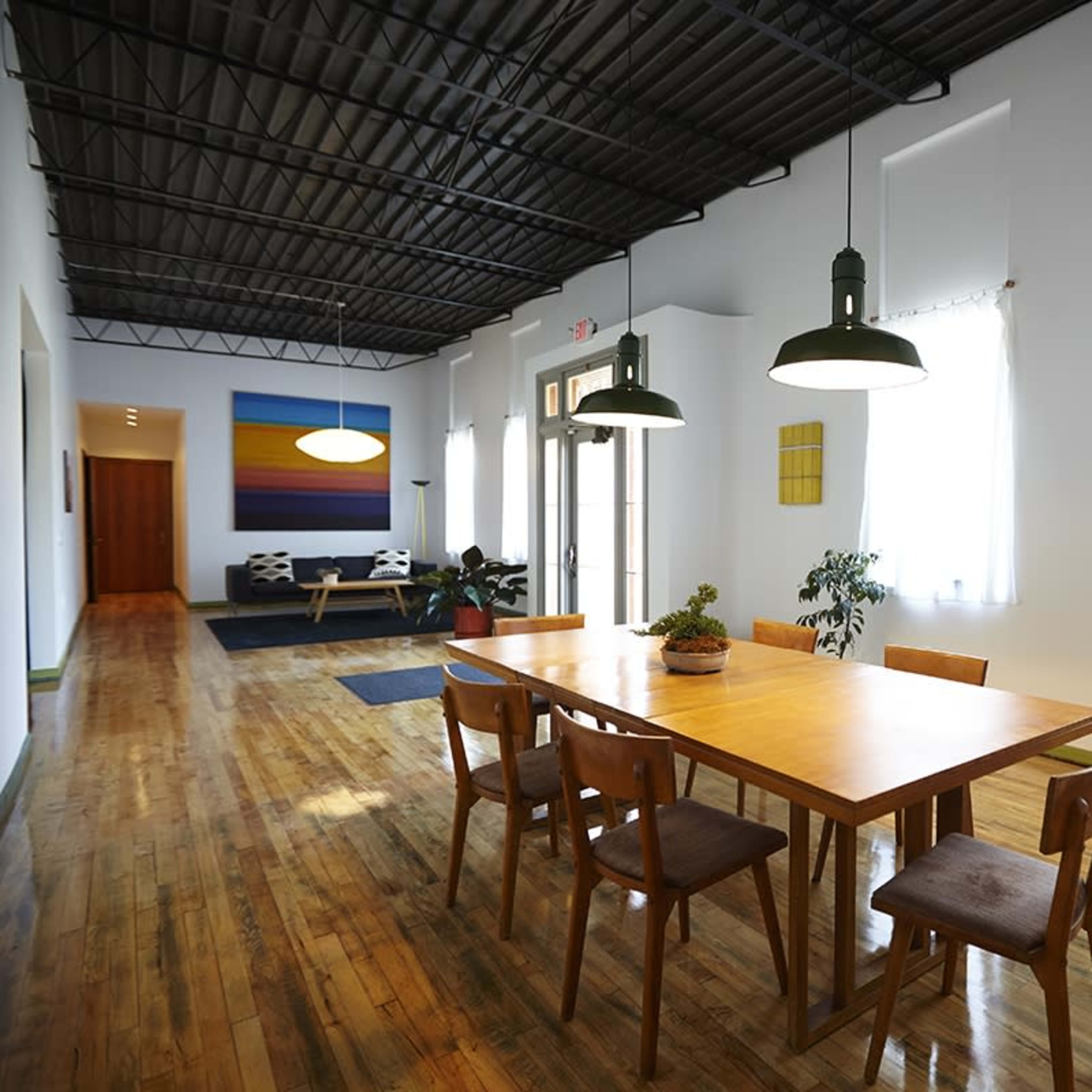 A spacious dining area features a long wooden table surrounded by chairs, with large windows allowing natural light to fill the room.