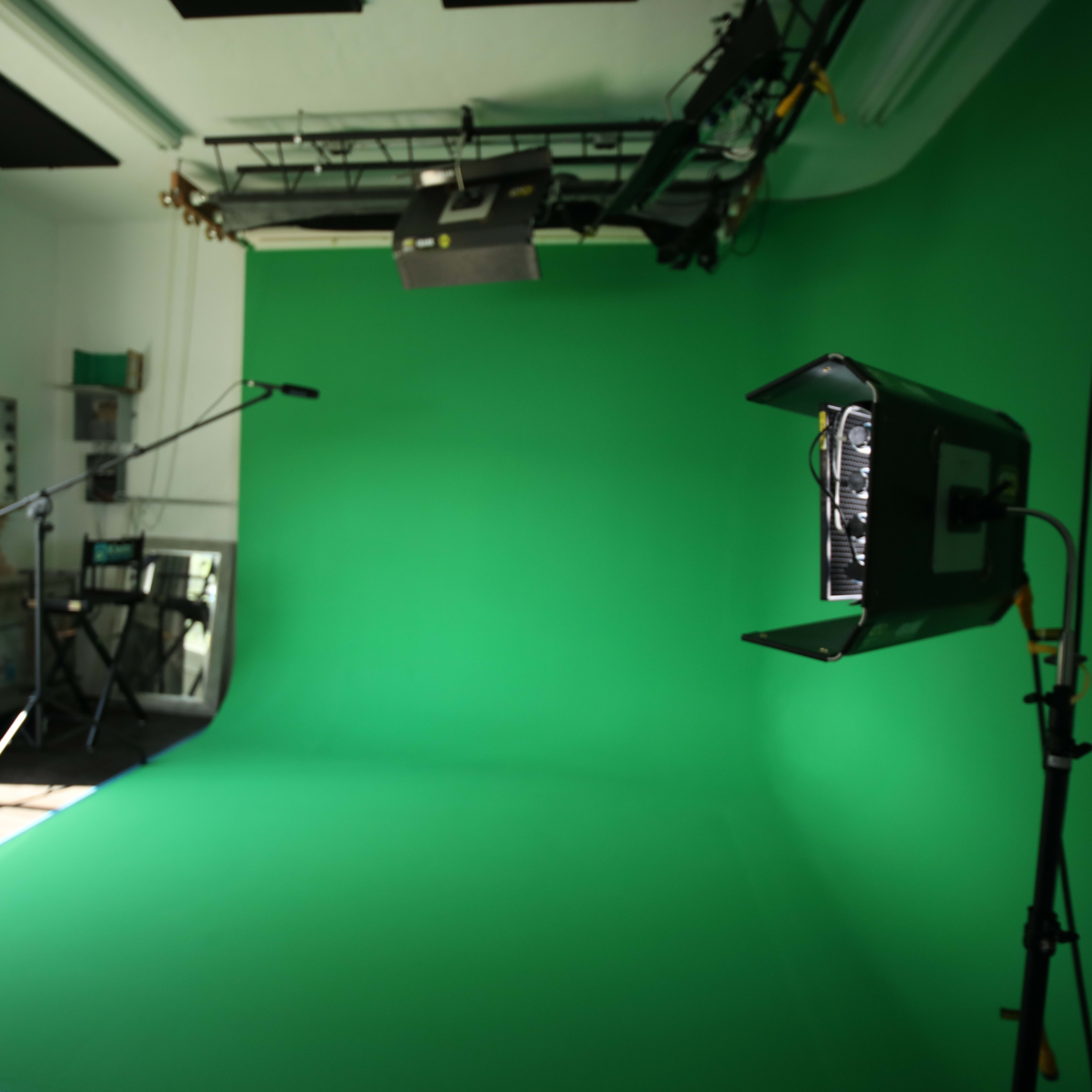 A photography studio with a green screen backdrop, lighting equipment, and a microphone setup.