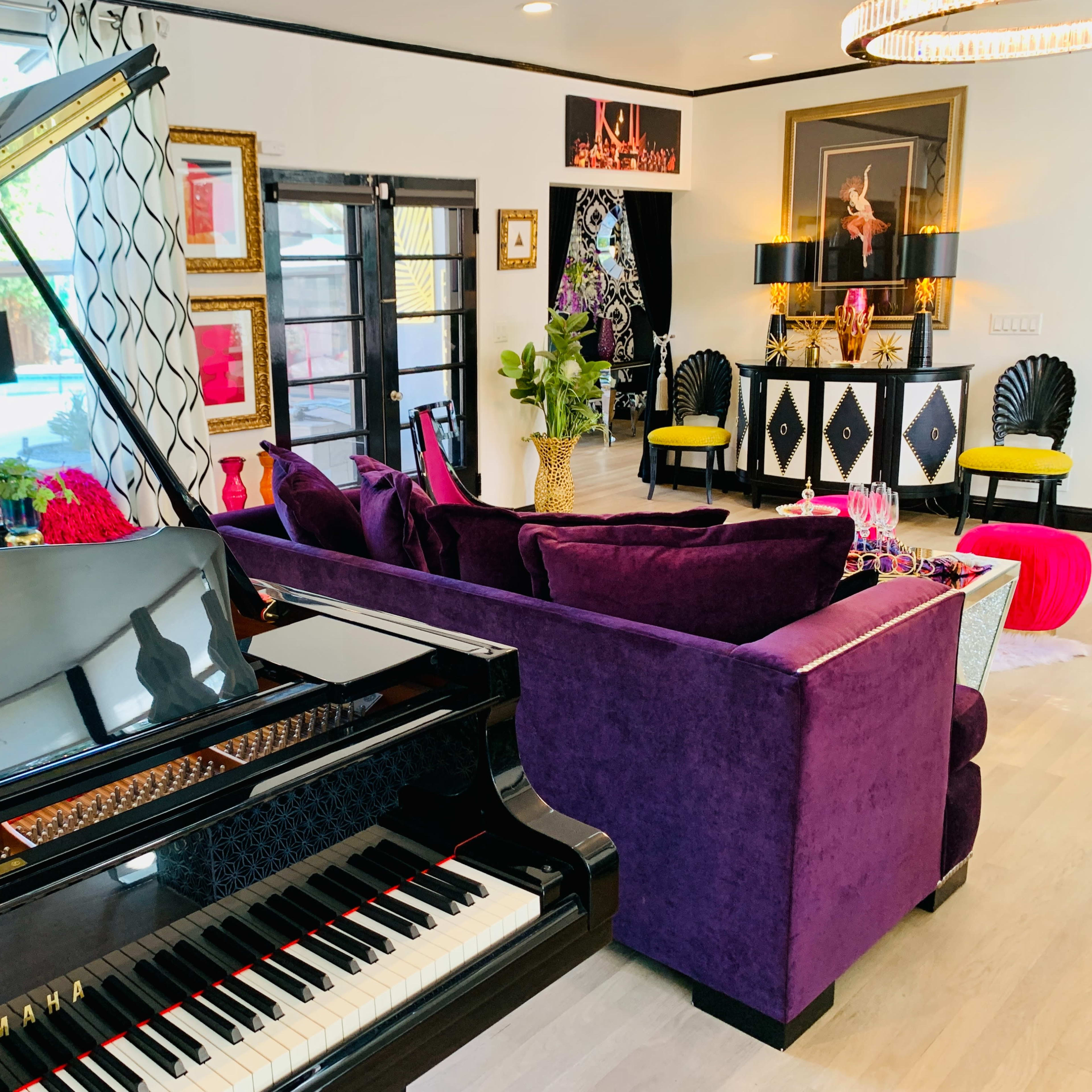 A black grand piano is positioned in the foreground of a modern living room featuring purple couches and vibrant decor.