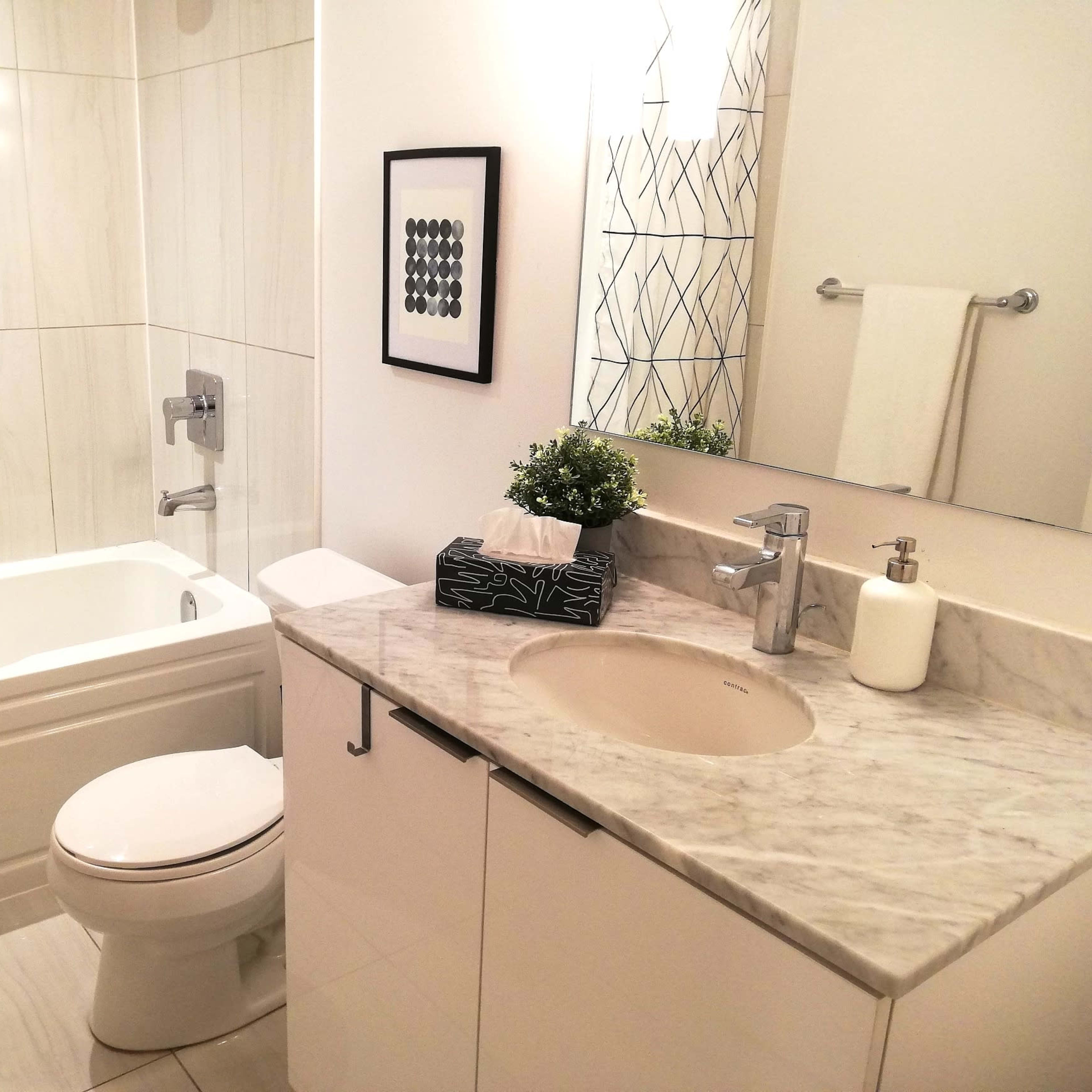 A modern bathroom featuring a bathtub with a shower, a sink with a marble countertop, and a decorative mirror.