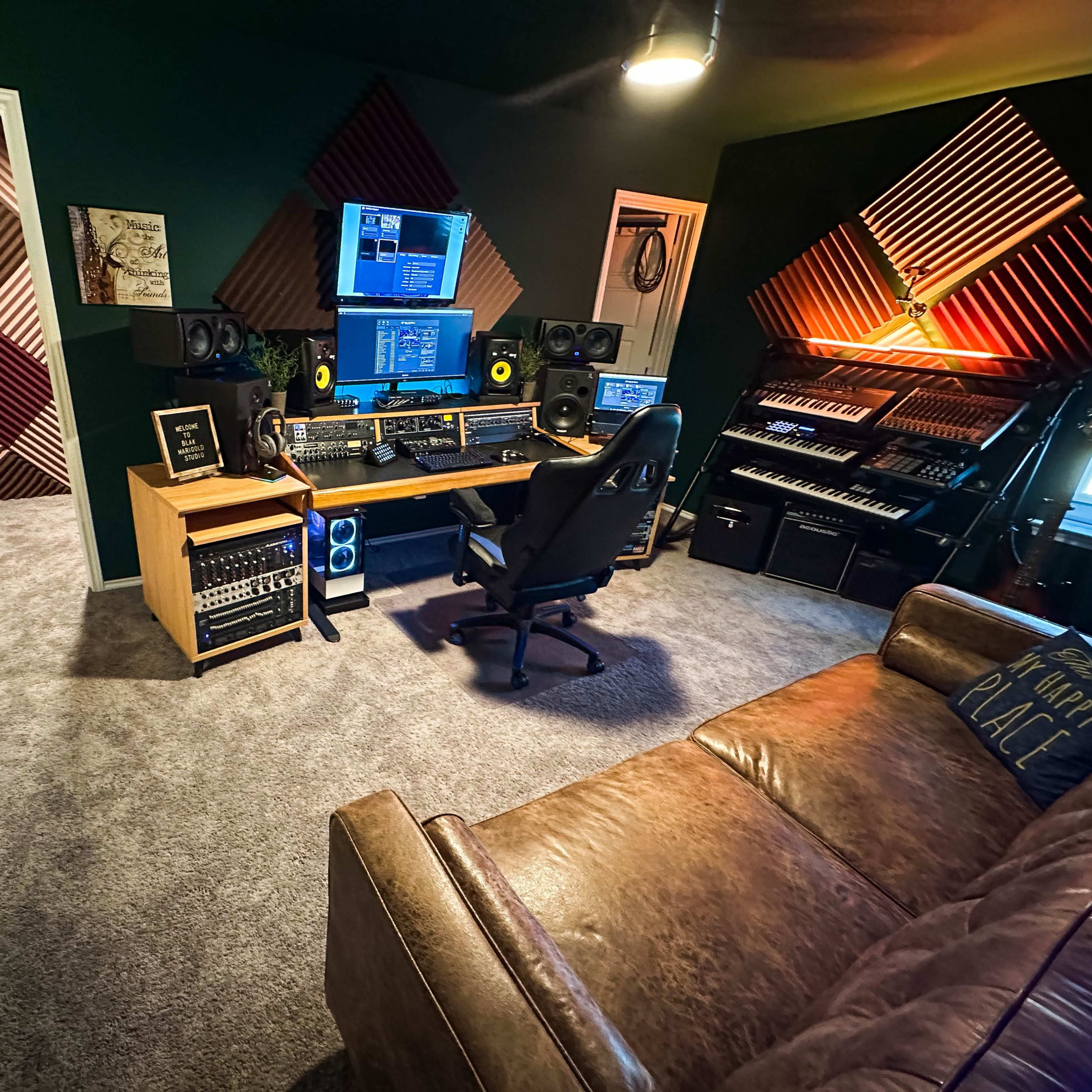 A music production studio featuring a central workstation with audio equipment, monitors, and a comfortable seating area.