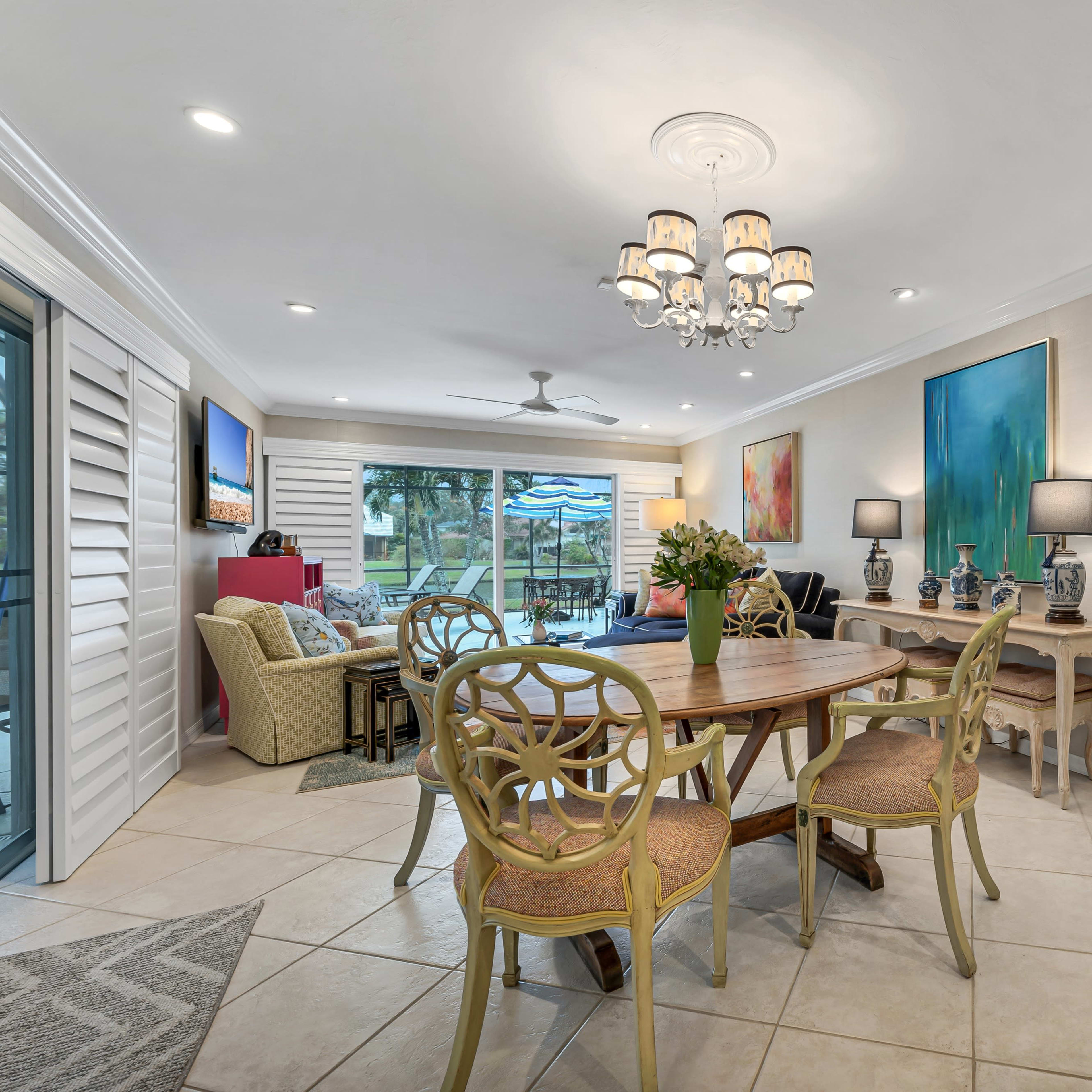 A modern living space with a dining table and chairs, a chandelier, and large windows that overlook a pool area.