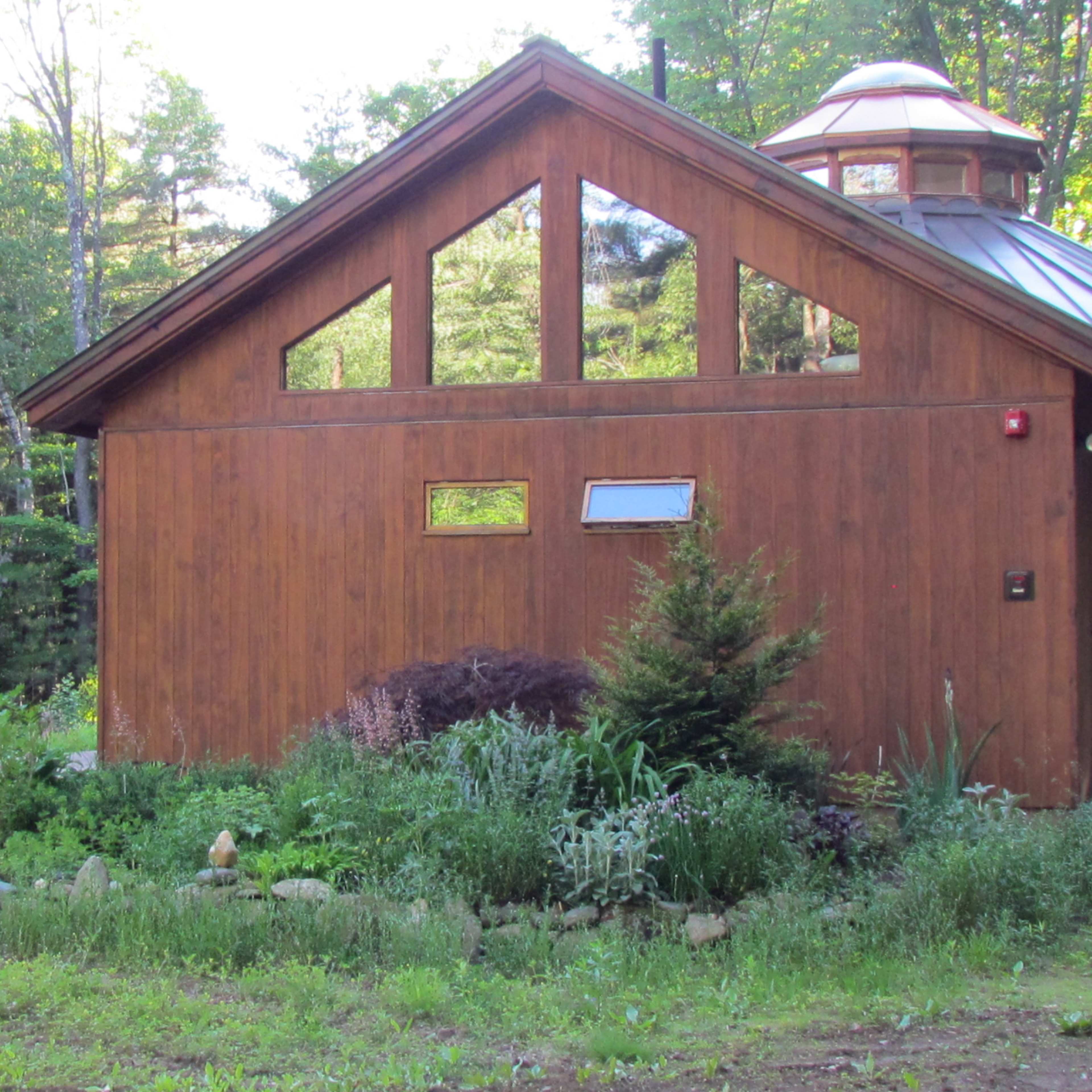 A wooden cabin surrounded by a garden and trees in a wooded area.