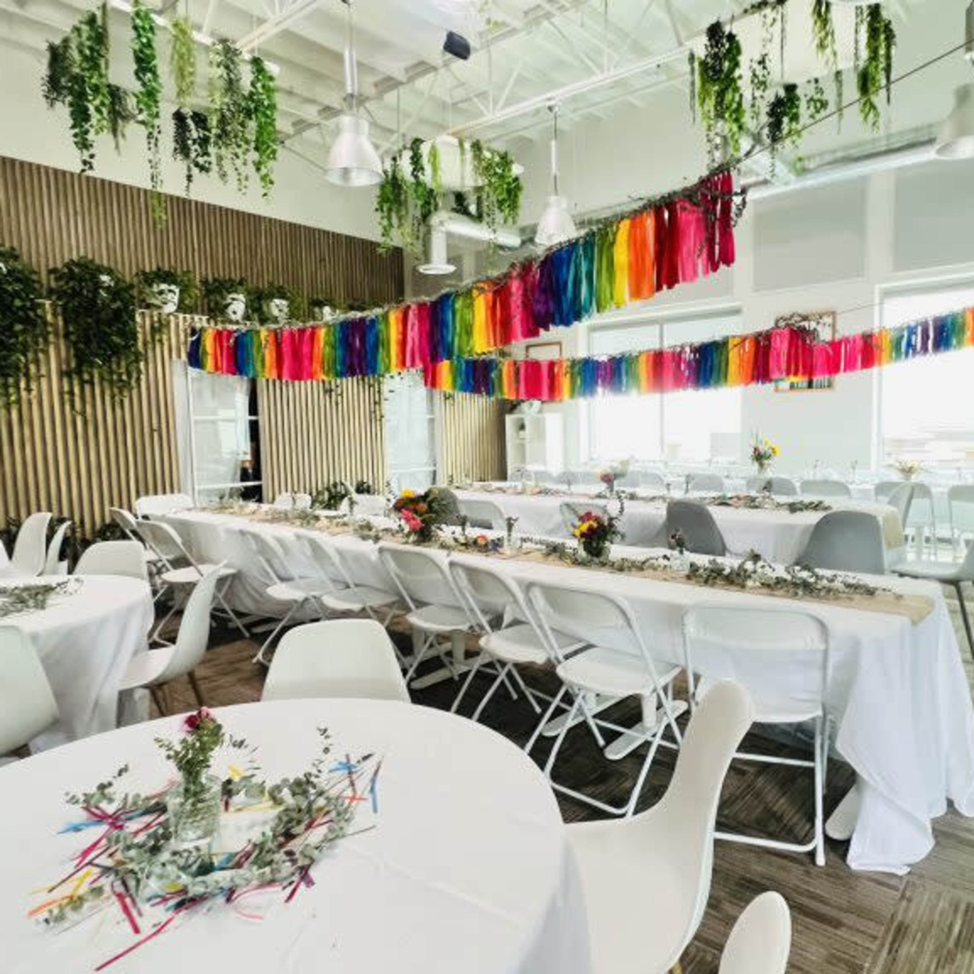 A bright, modern event space decorated with colorful streamers and tables set for a gathering.