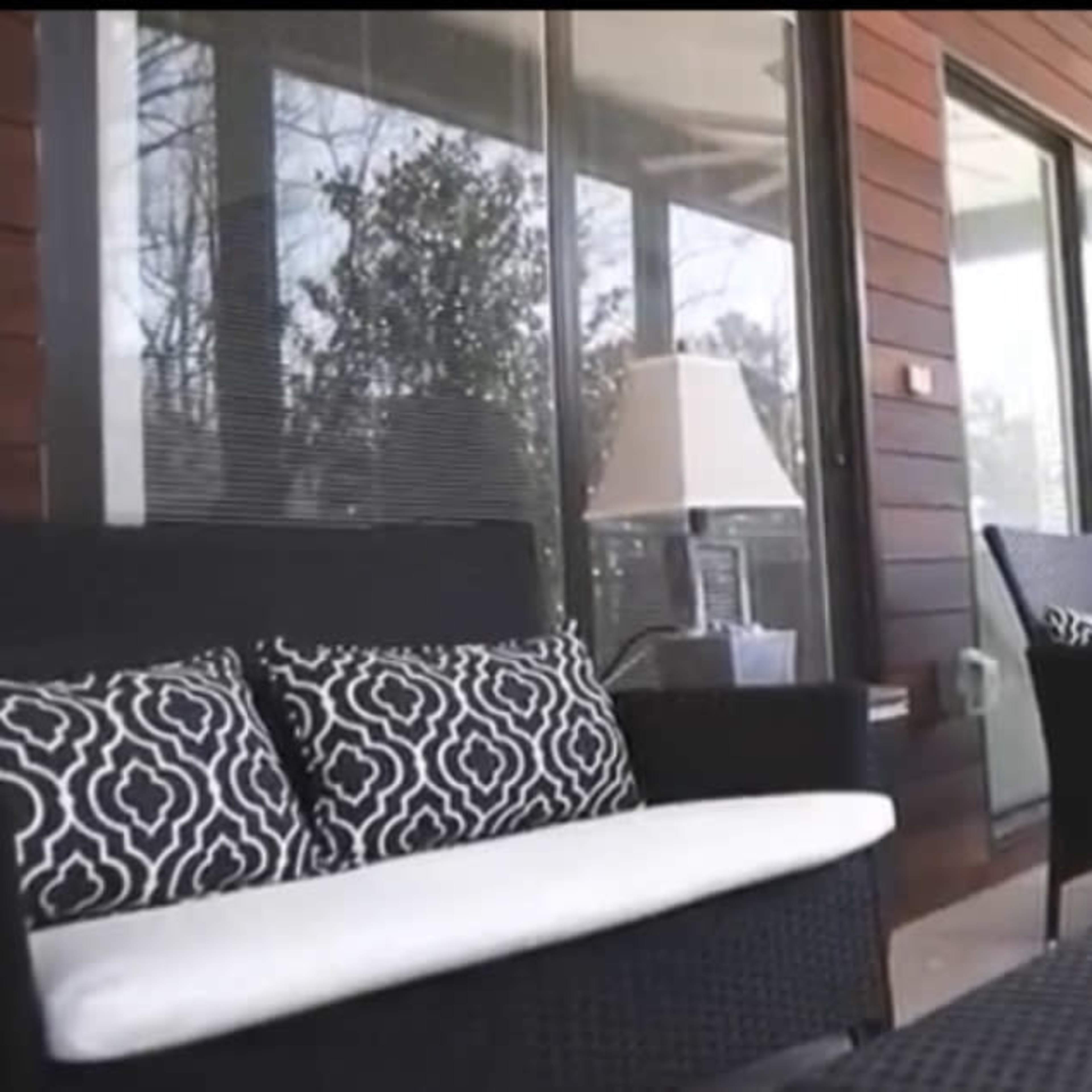 A modern outdoor seating area with wicker furniture, a decorative bowl on the table, and large windows overlooking a forested view.