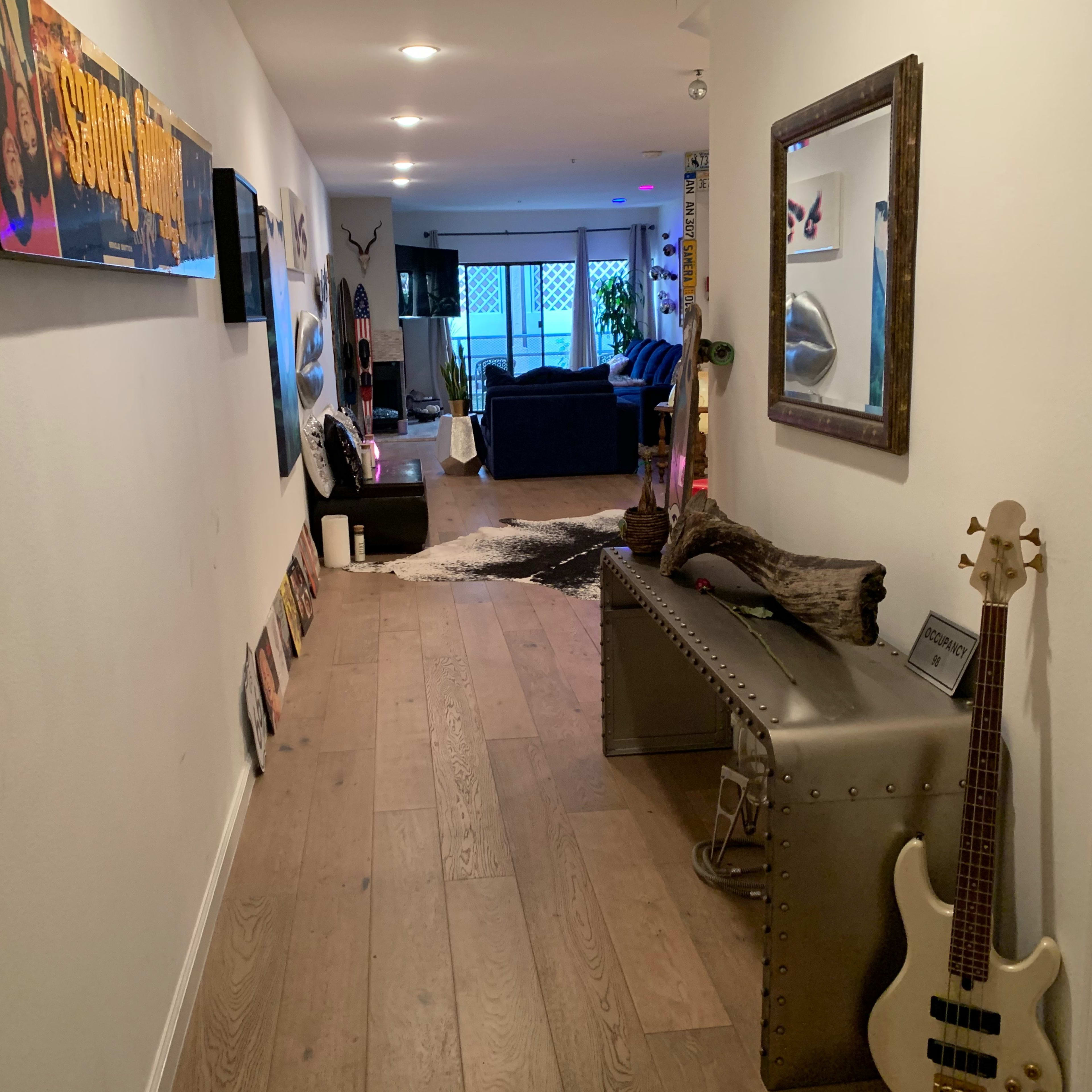 A hallway with light wooden flooring leads to a cozy living area, featuring a couch, wall decorations, and a music-themed display.