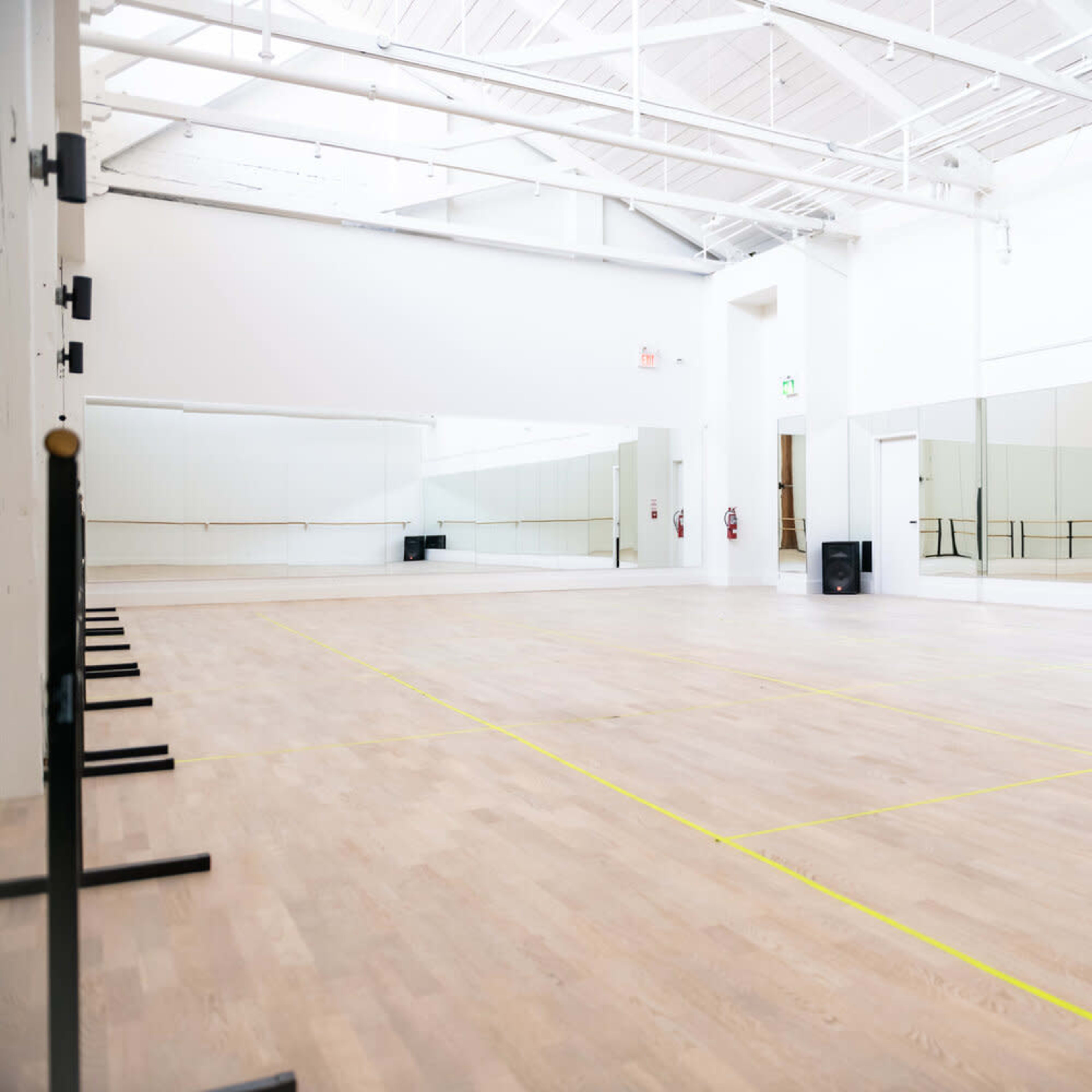 An empty dance studio with wooden flooring, large mirrors on one wall, and ballet barres along the other.
