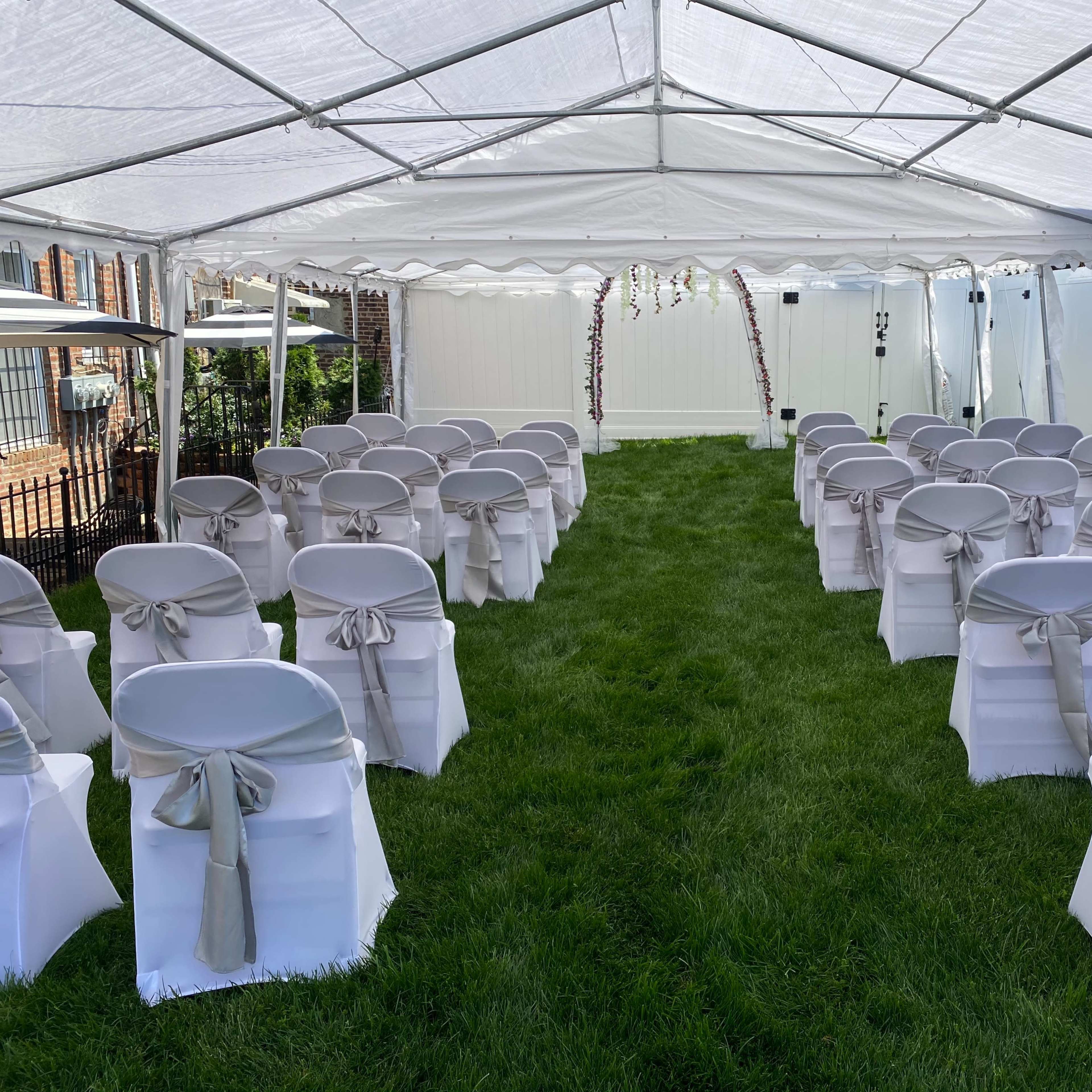 A white tent set up on grass, with rows of chairs arranged in two facing sections, each chair tied with a light-colored ribbon.