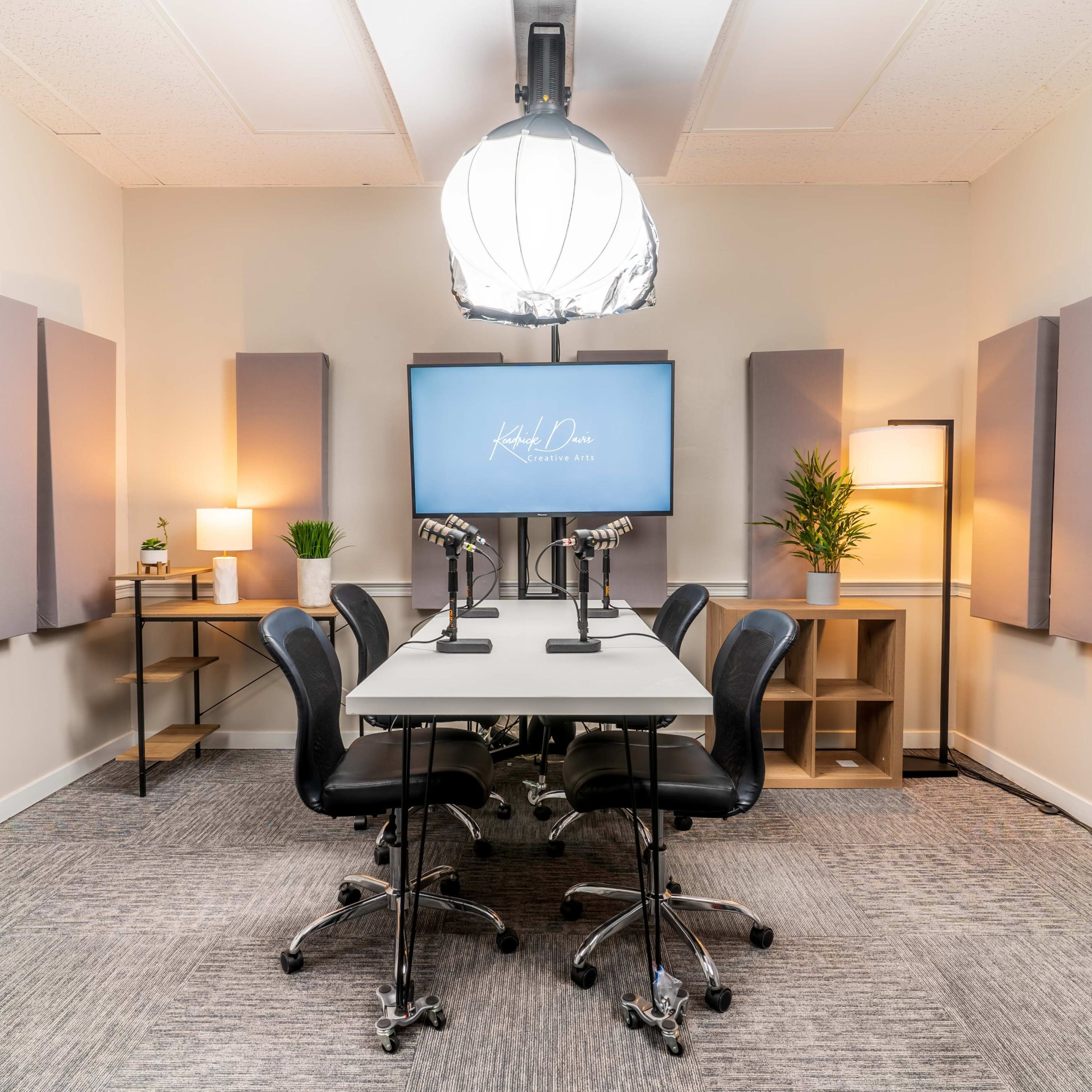 A modern conference room equipped with a central table, four black chairs, a large screen, and soundproof wall panels.