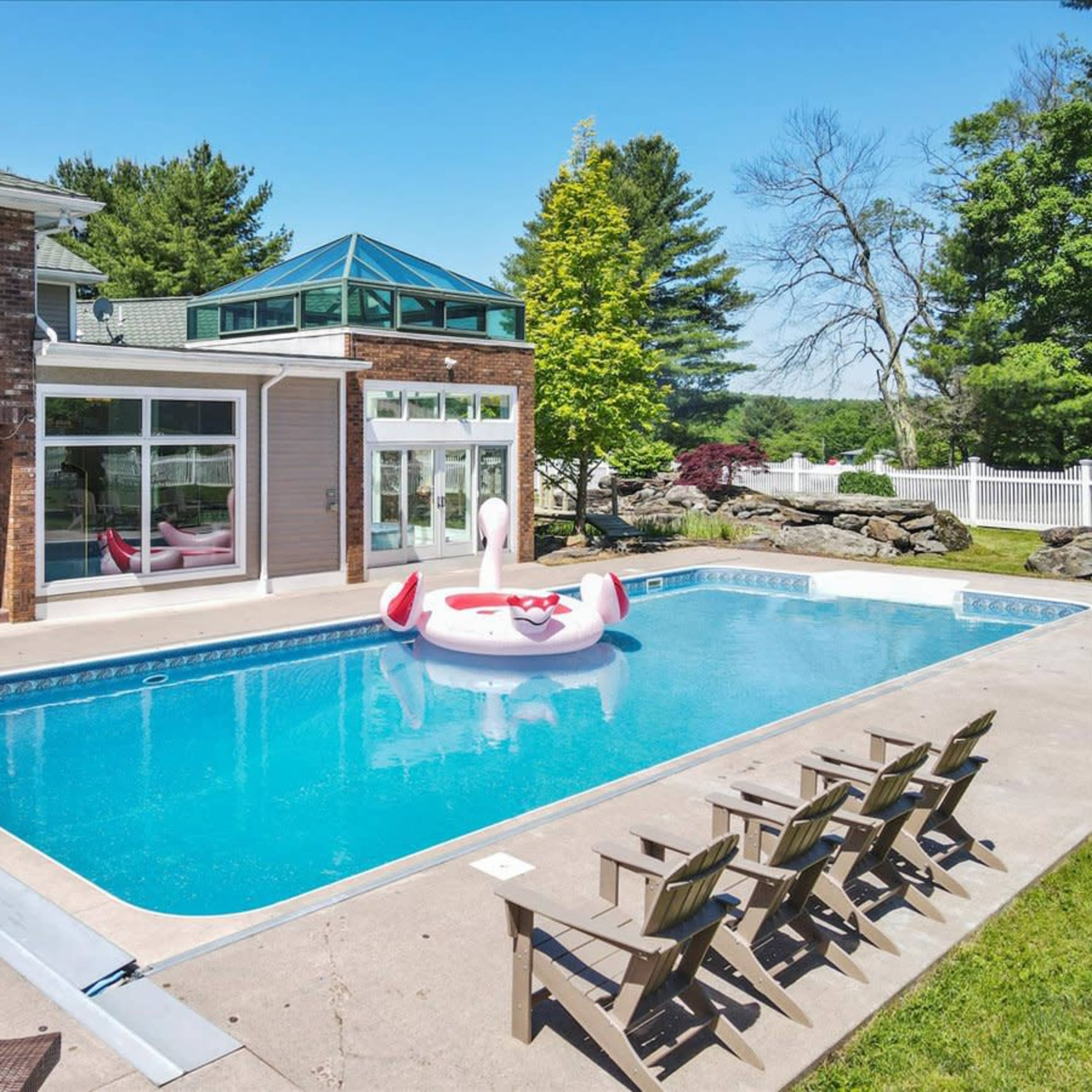 A large swimming pool surrounded by lounge chairs, featuring a float in the shape of a swan in the center, with a modern house in the background.