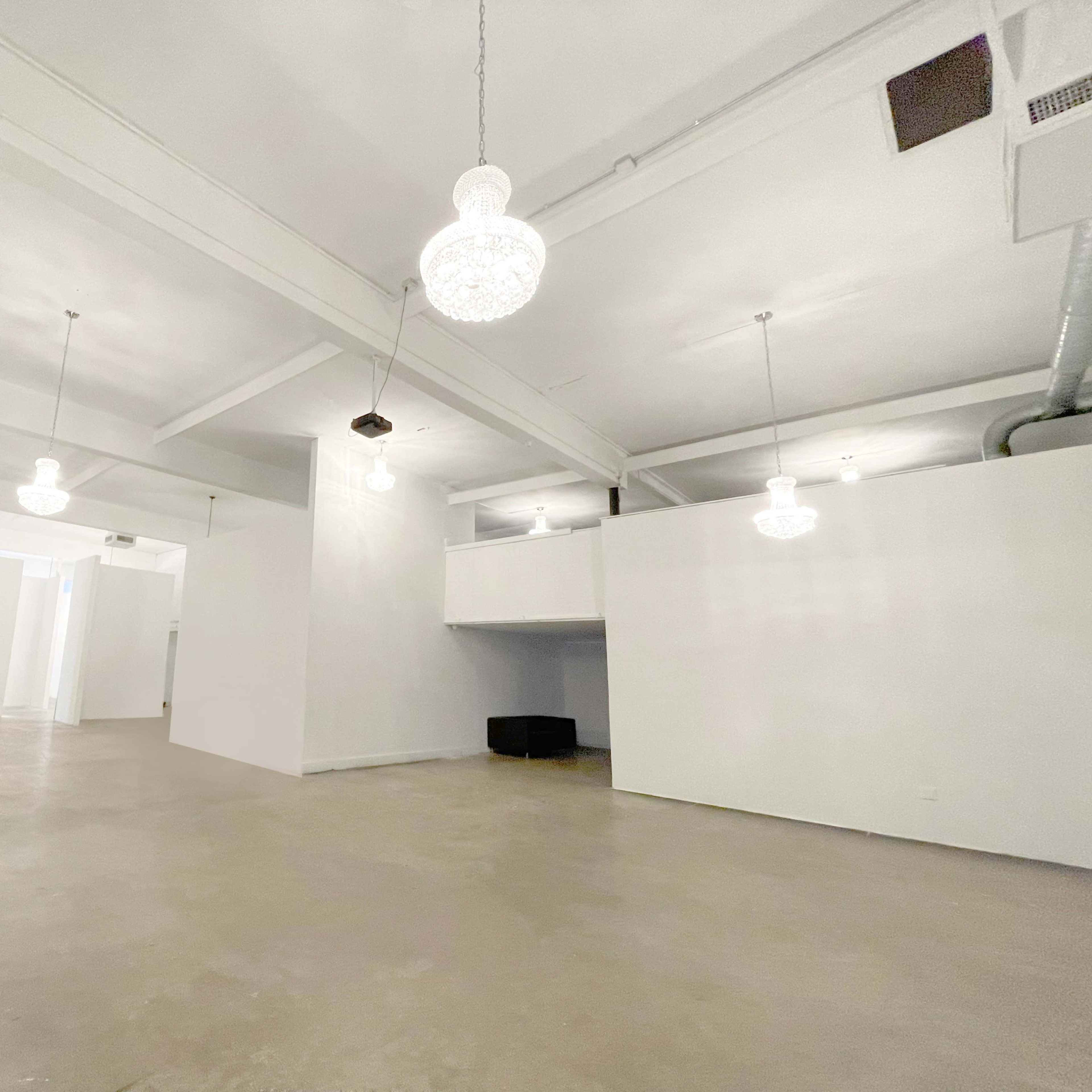 A spacious, empty room with white walls and ceiling, featuring several hanging light fixtures and concrete flooring.