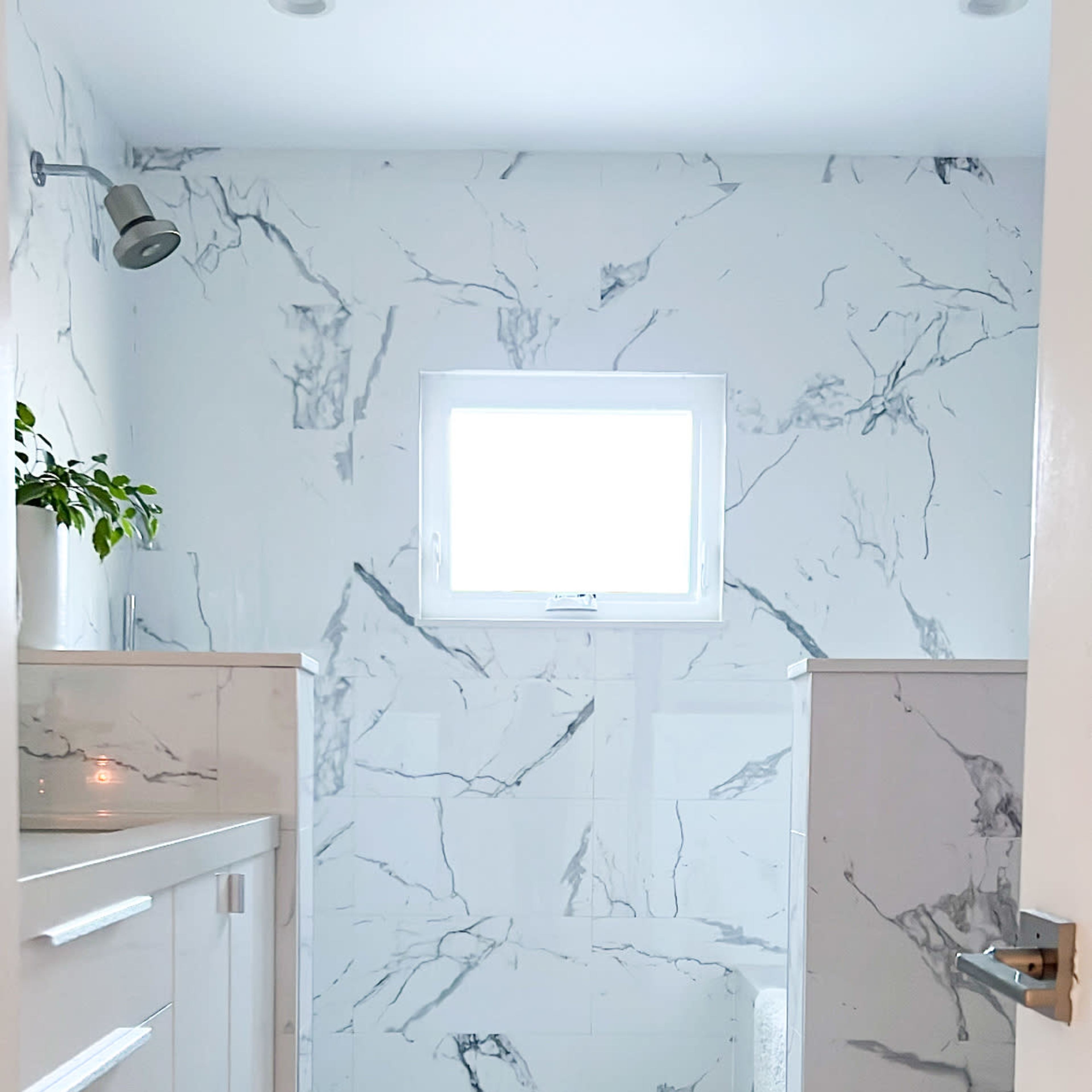 A bathroom featuring marble-patterned walls, a shower area with a clear wall, a window, and a decorative bath mat at the entrance.