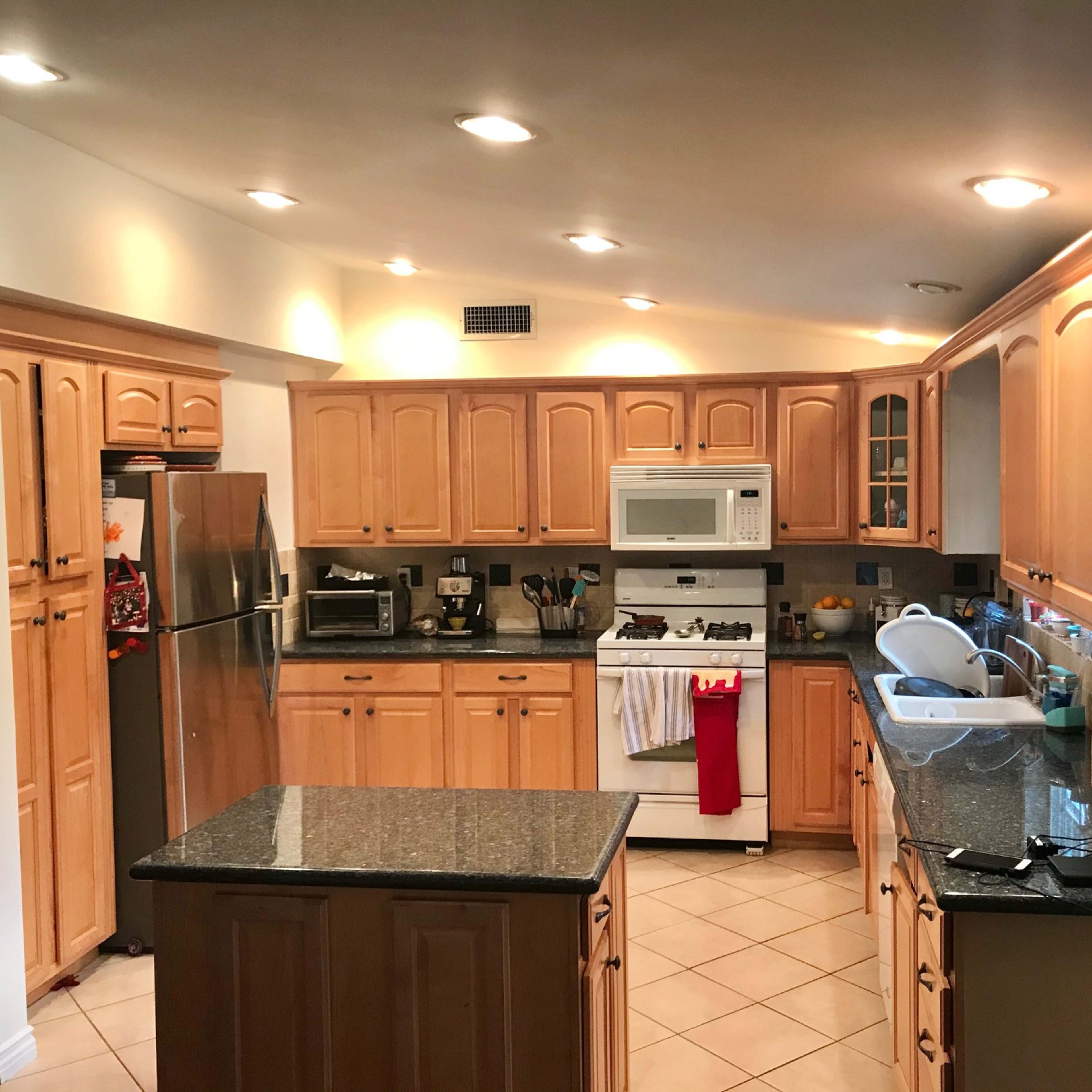 The kitchen features wooden cabinetry, a stainless steel refrigerator, a gas stove, a microwave, and an island with a dark granite countertop.