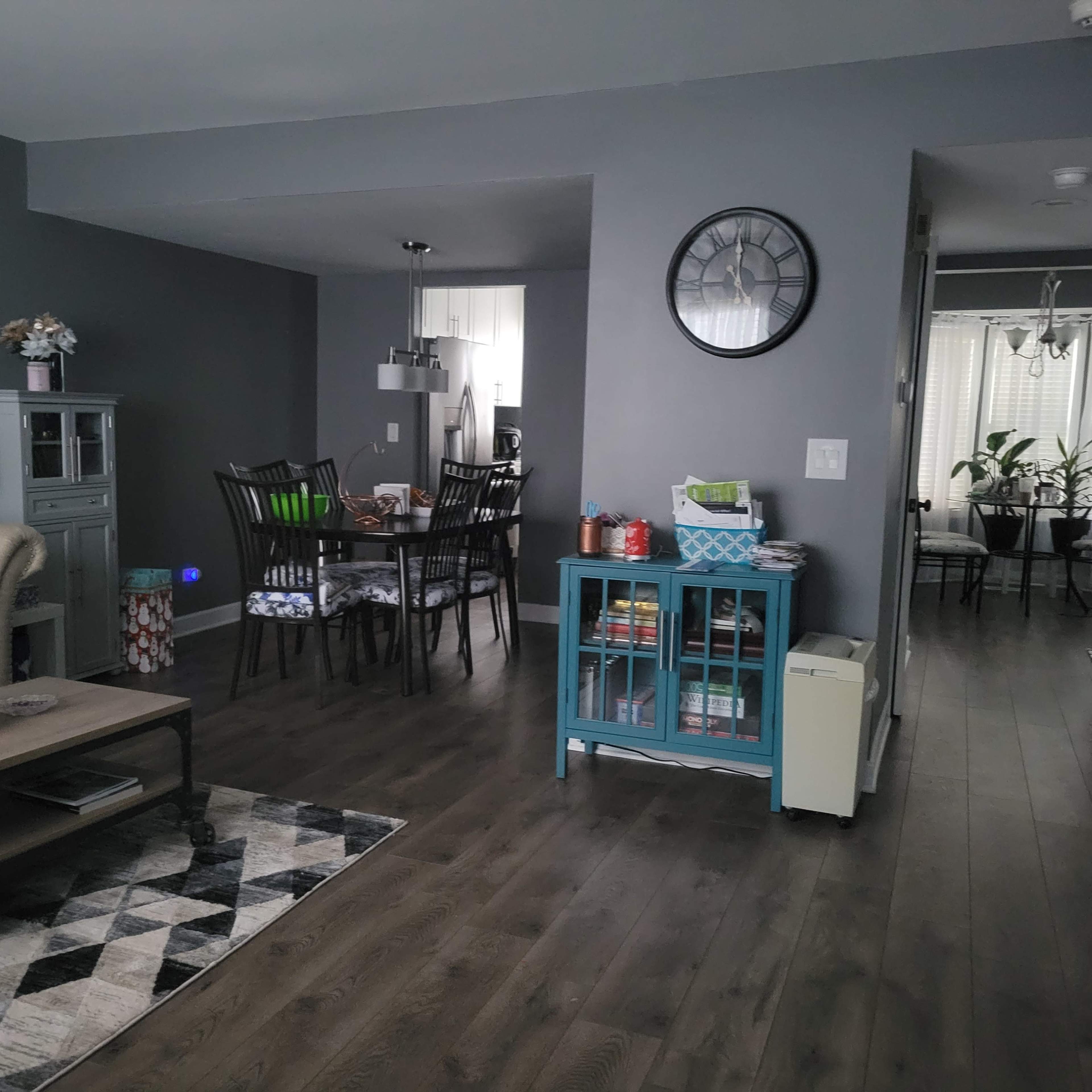 A modern living space featuring a sofa, dining area with a table and chairs, and a hallway leading to another room, all with gray walls and wooden flooring.