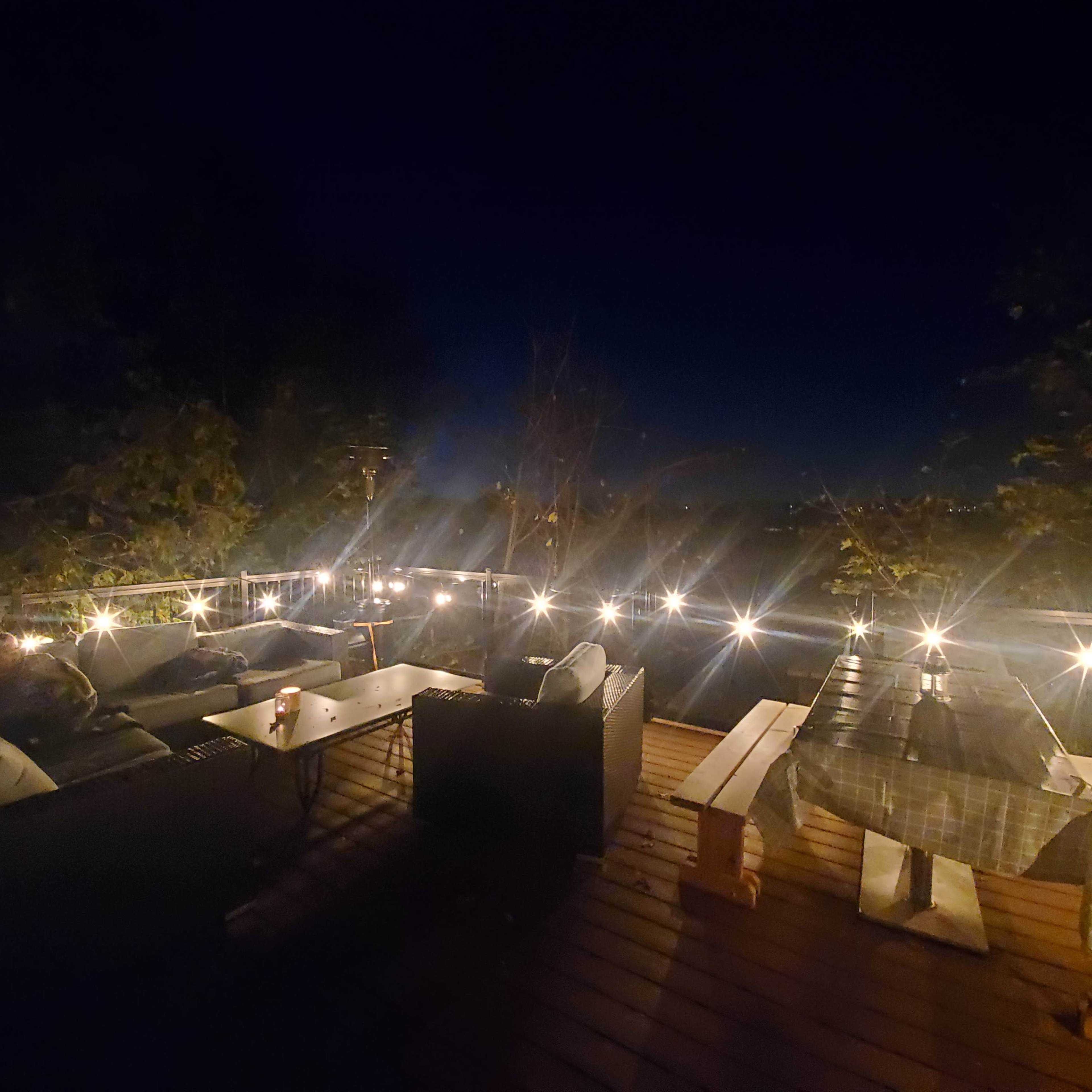 The scene shows a wooden deck at night with sofas and a table illuminated by string lights.