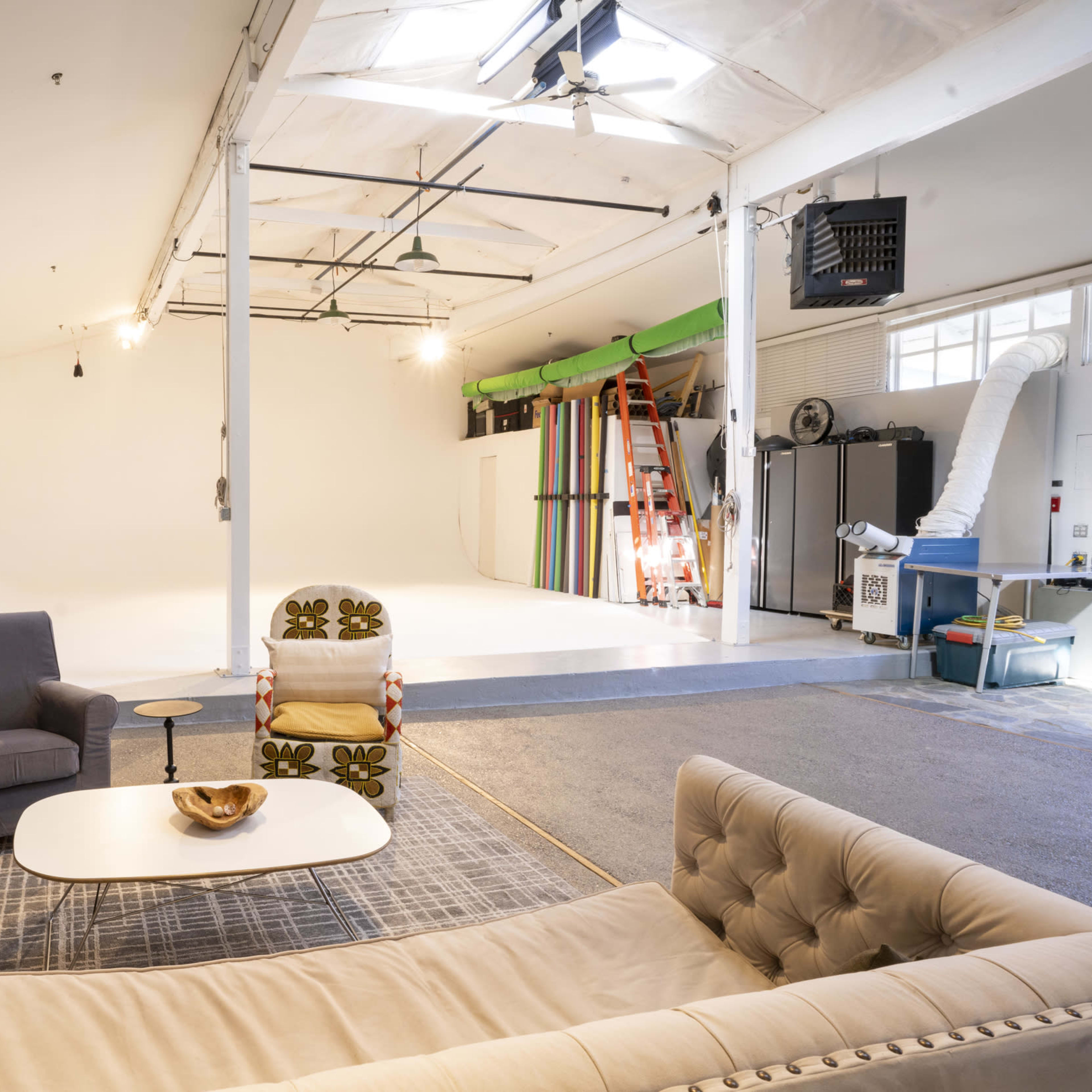 A spacious photo studio features a large white backdrop, a seating area with a sofa and chairs, and various studio equipment along the walls.