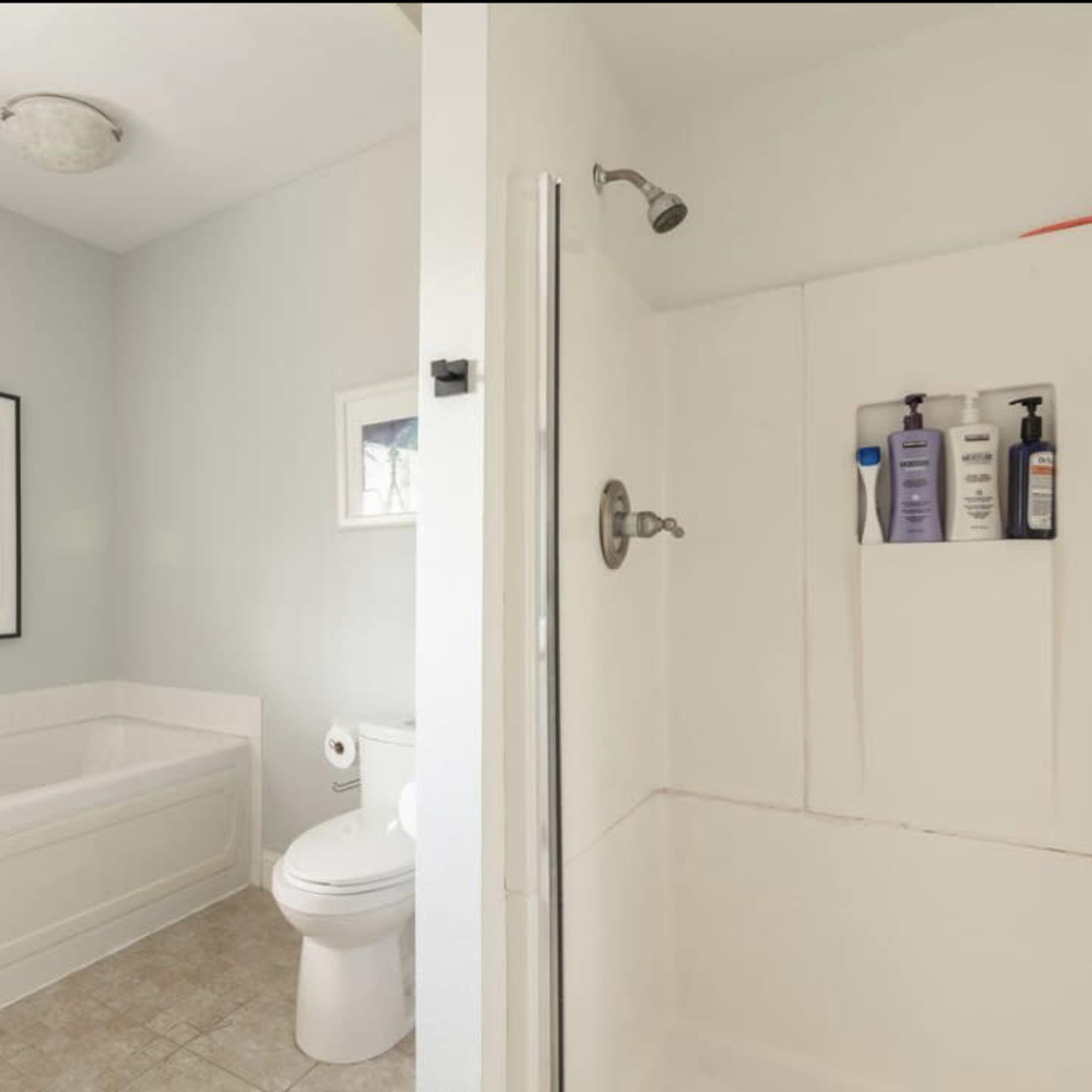 A bathroom featuring a tub, a shower area, a toilet, and a small bench with a planter.