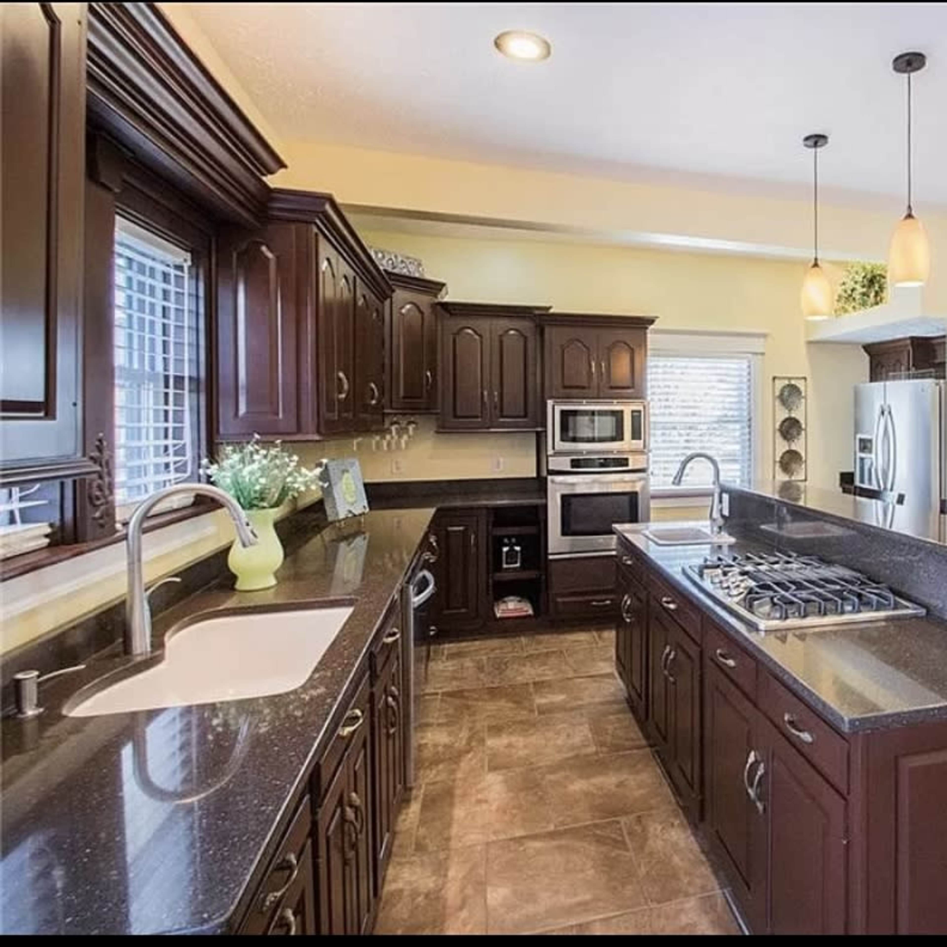 A spacious kitchen featuring dark wooden cabinets, stainless steel appliances, and a large countertop with a gas stove.