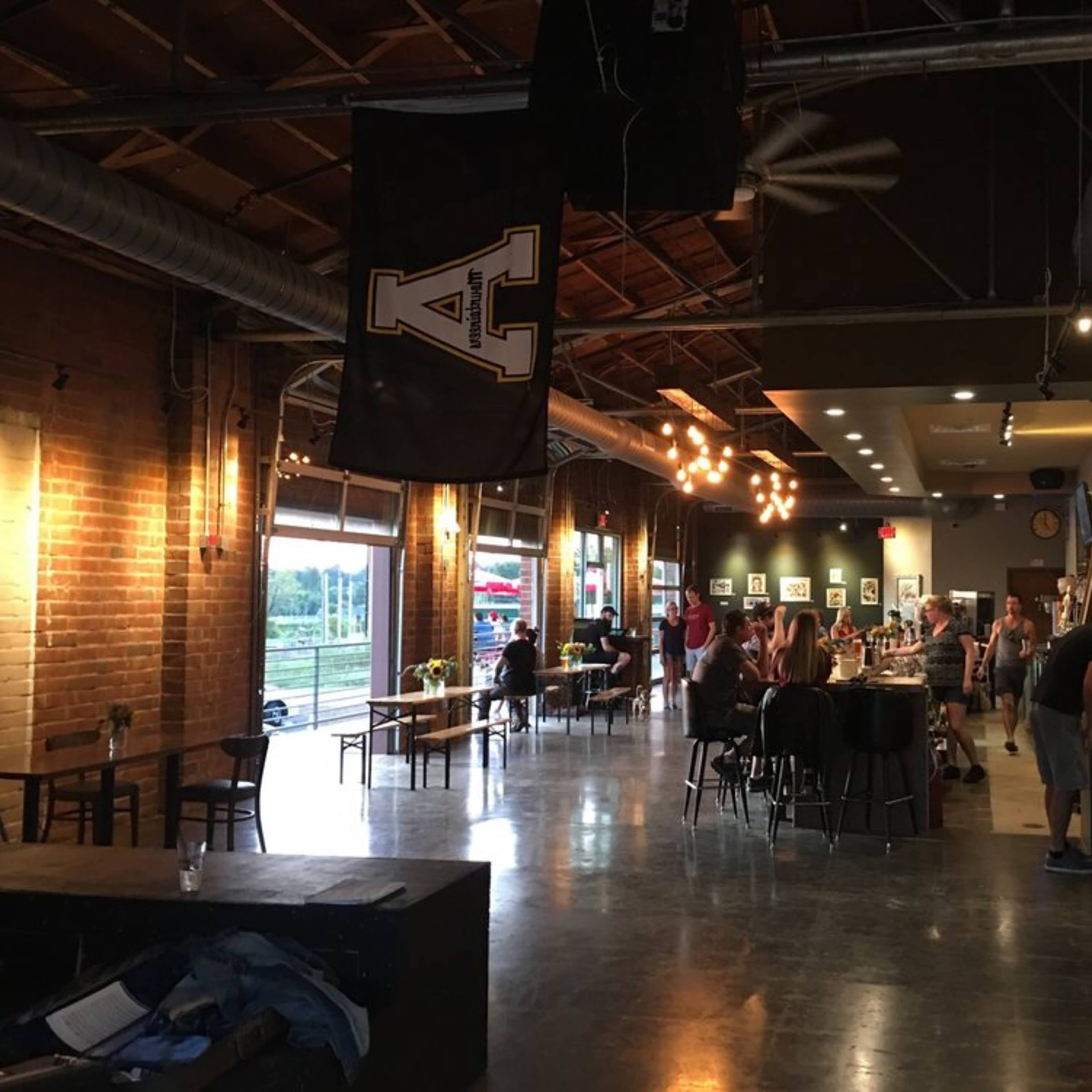 A spacious, industrial-style café with brick walls, wooden tables, and a few people seated or lining up at the counter.