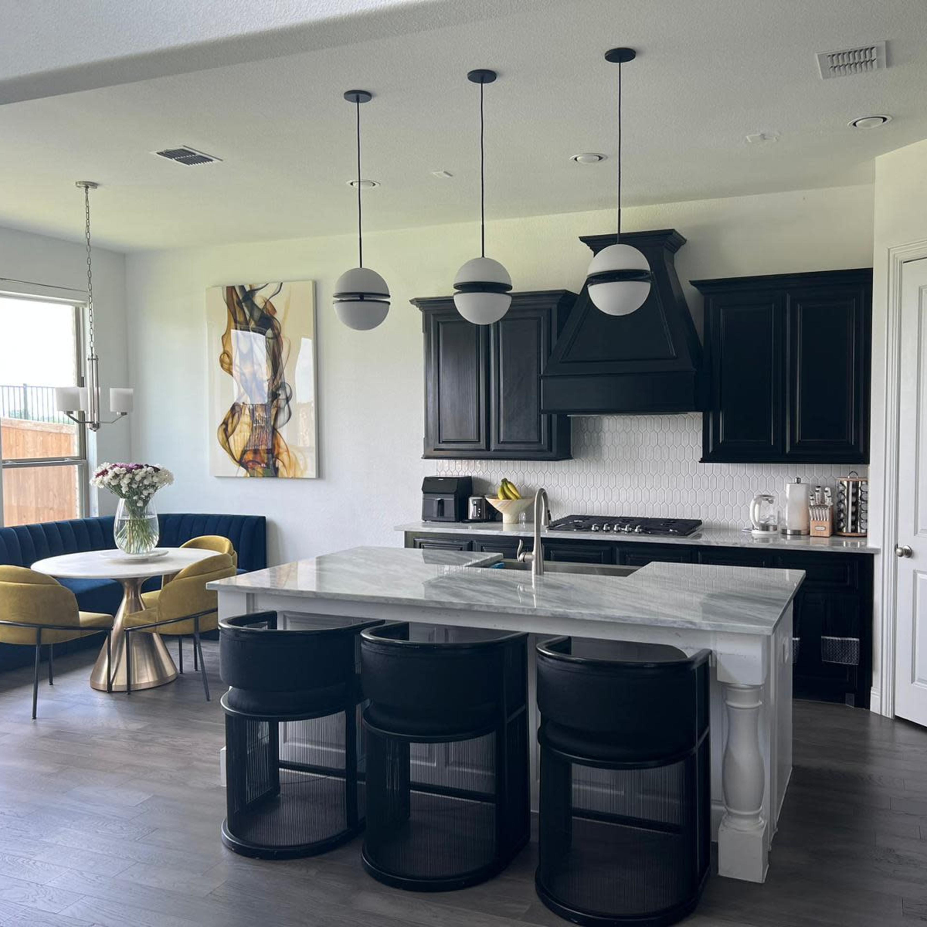 A modern kitchen with black cabinetry, a marble island, and a dining area featuring a circular table and yellow chairs.