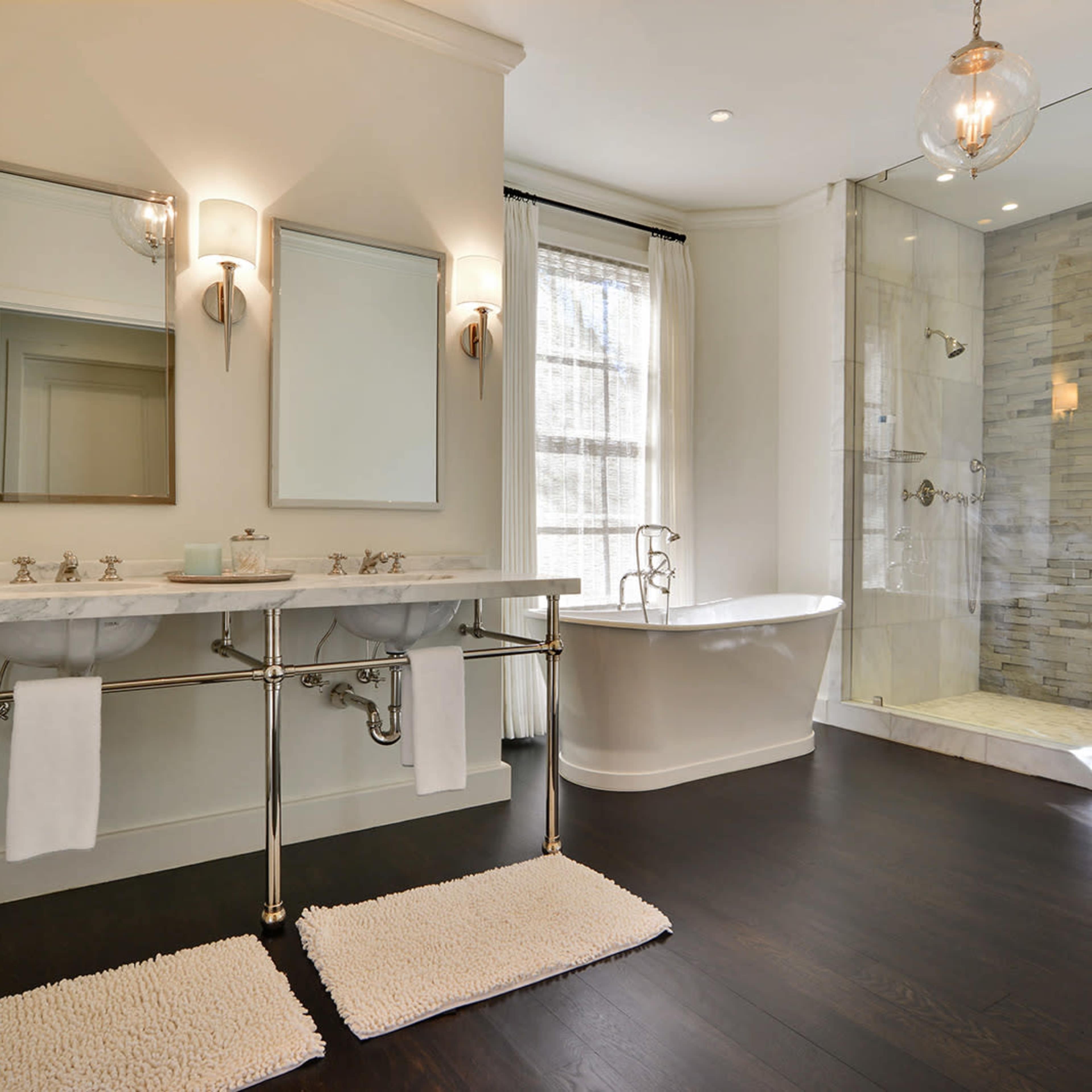 The bathroom features dual sinks, a freestanding tub, and a glass-enclosed shower with stone walls.