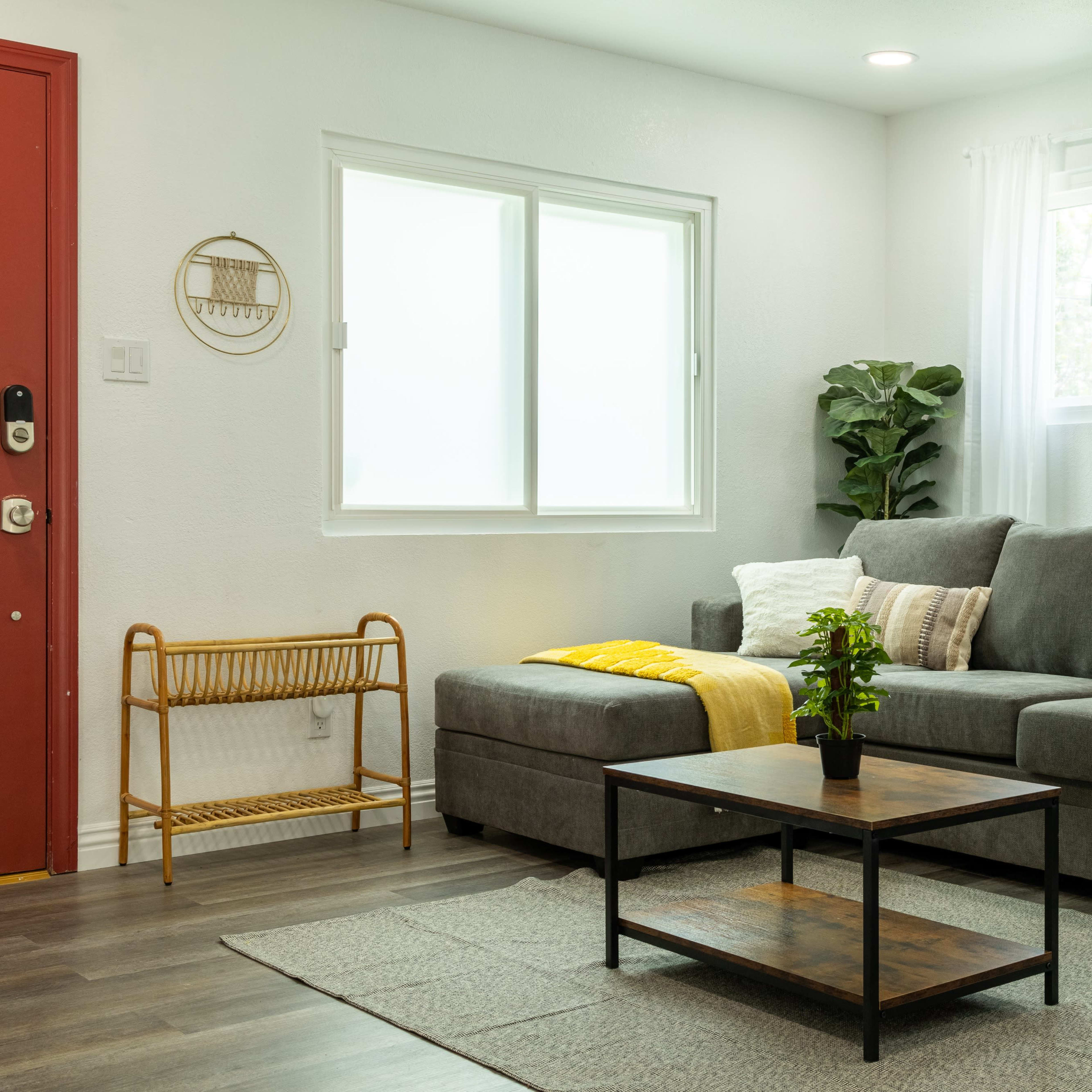 A living room features a gray sectional sofa, a wooden coffee table, and a side table with plants near a window.