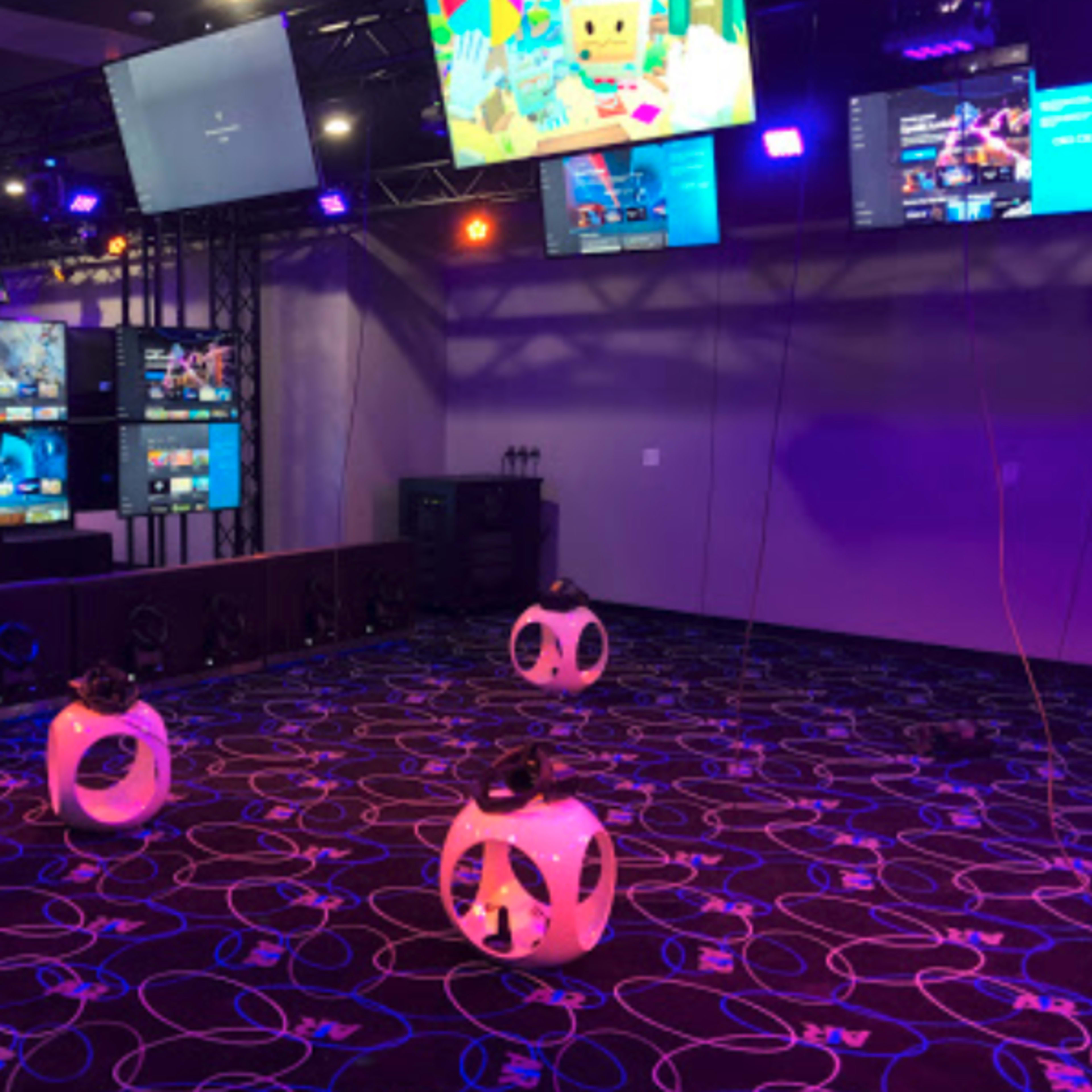 A gaming room equipped with multiple screens and three virtual reality headsets placed on the floor.
